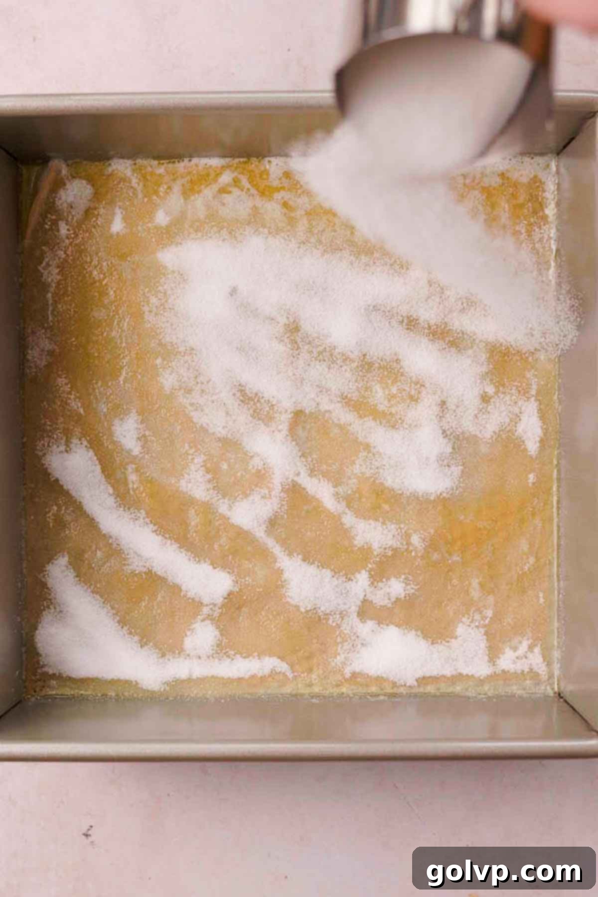 A square baking pan with a shimmering layer of melted butter at the bottom, evenly sprinkled with granulated sugar, ready for lemon slices.