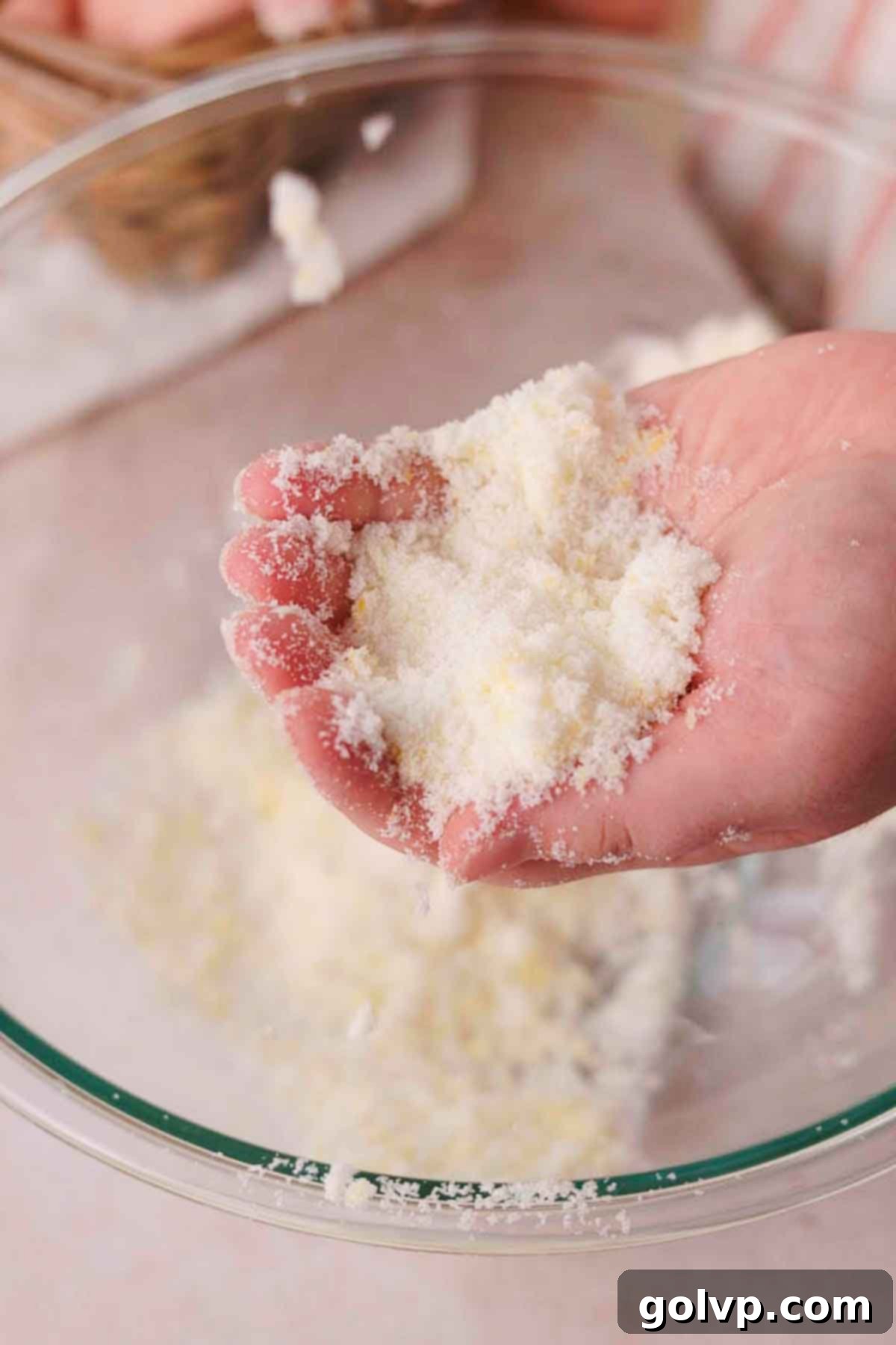 Hands vigorously rubbing lemon zest and granulated sugar together in a large glass bowl to release aromatic oils.