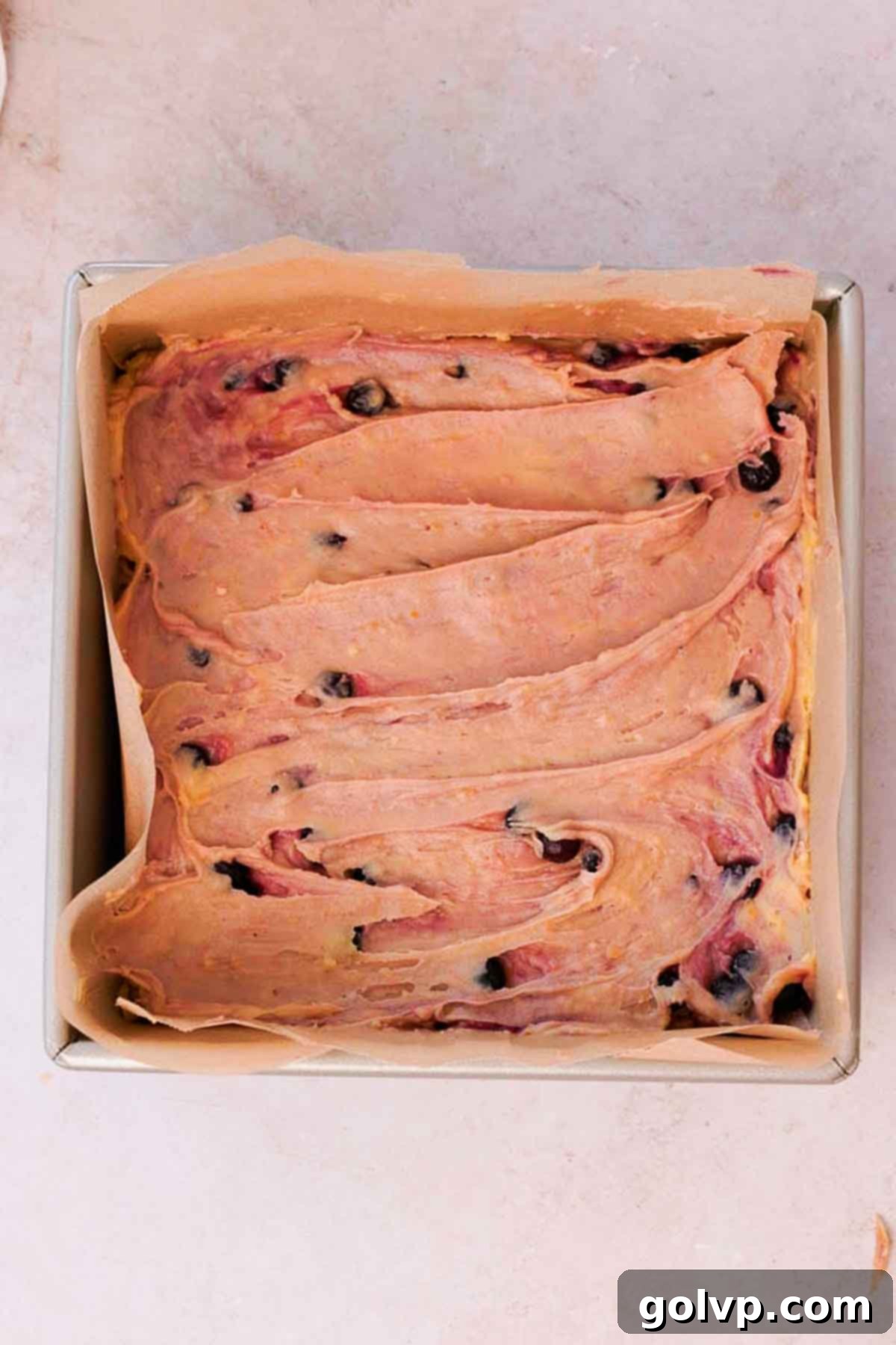 Smooth blueberry brownie batter spread evenly in a square baking pan lined with parchment paper