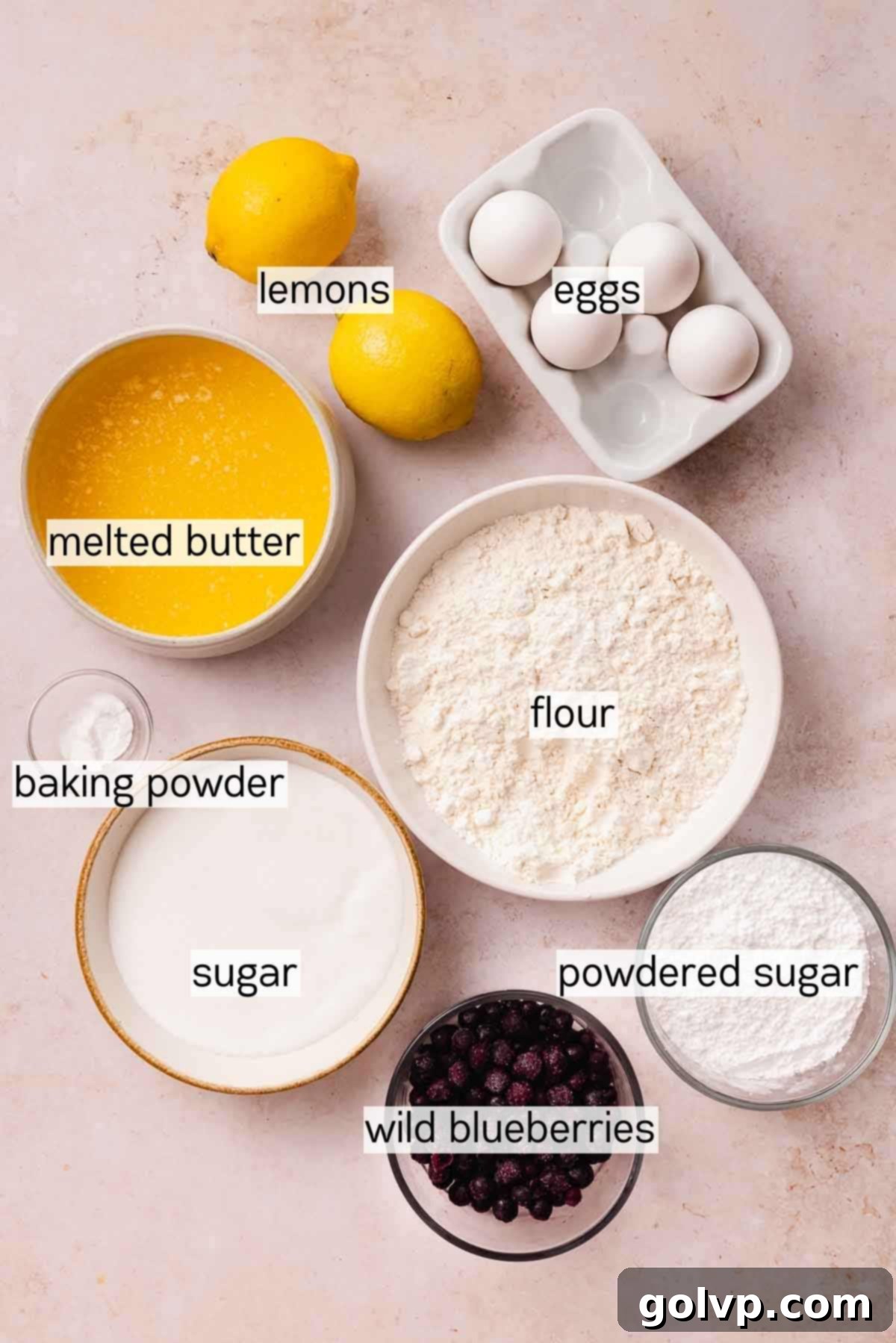 Bowls of key ingredients for blueberry lemon brownies, including lemons, blueberries, butter, eggs, flour, and sugar
