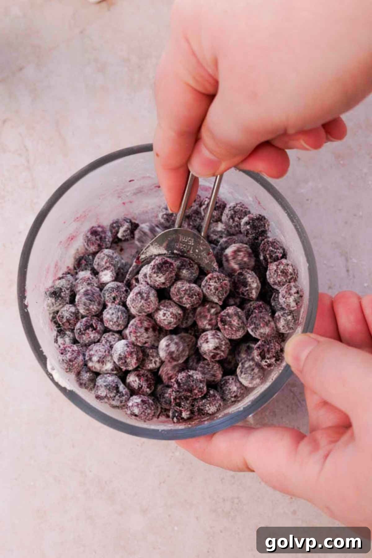 Mixing frozen wild blueberries with a tablespoon of flour in a small glass bowl, coating them to prevent sinking