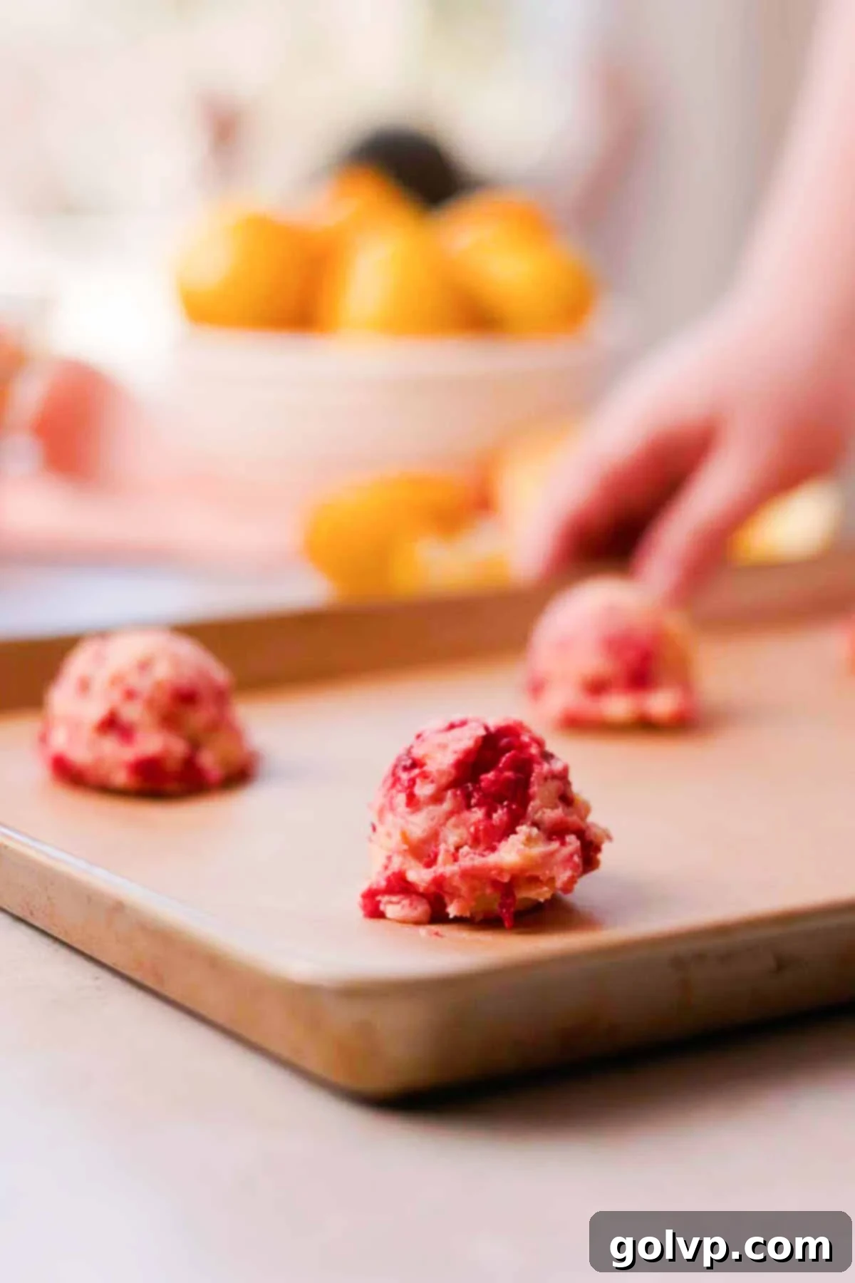Perfectly scooped balls of lemon raspberry cookie dough arranged on a parchment-lined baking sheet, ready for the oven
