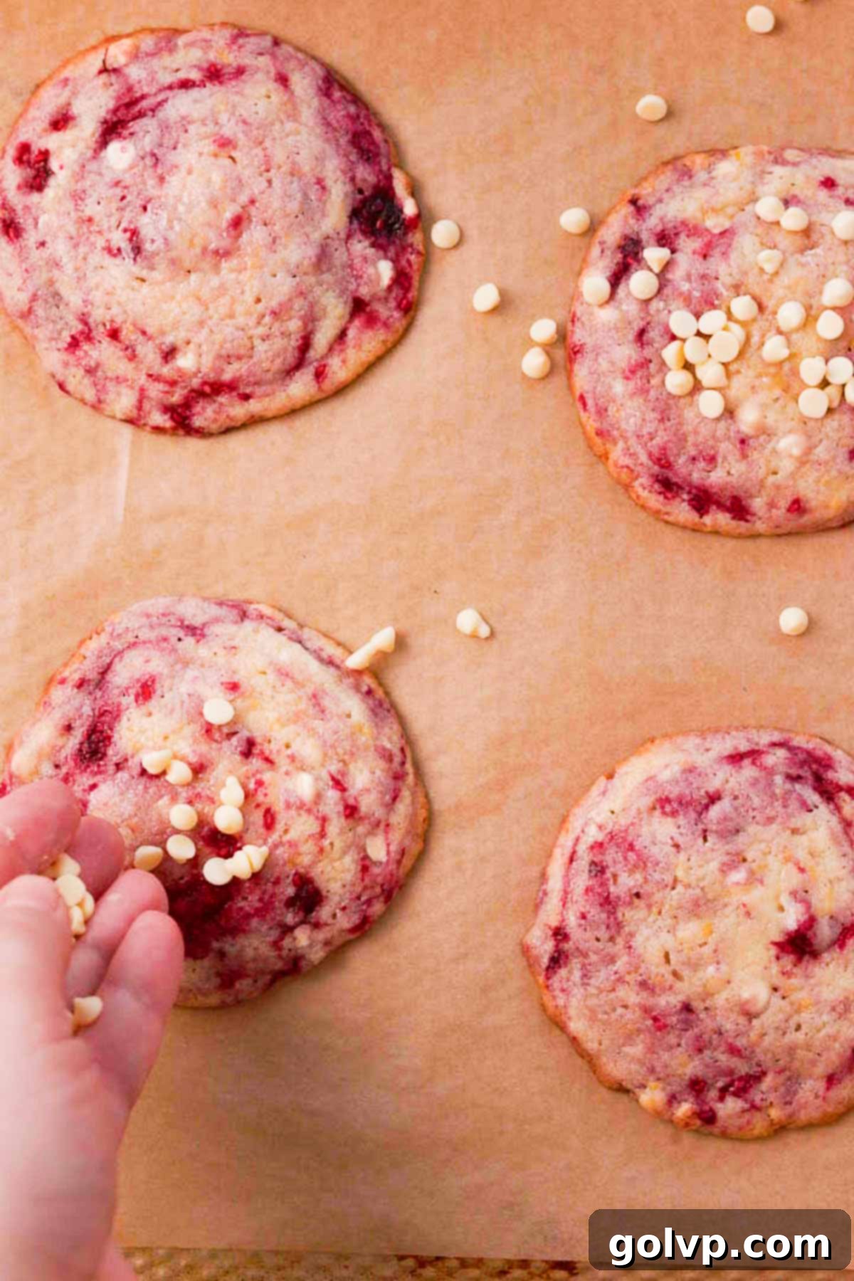 Sprinkling warm lemon raspberry cookies with more white chocolate chips and grated lemon zest after baking