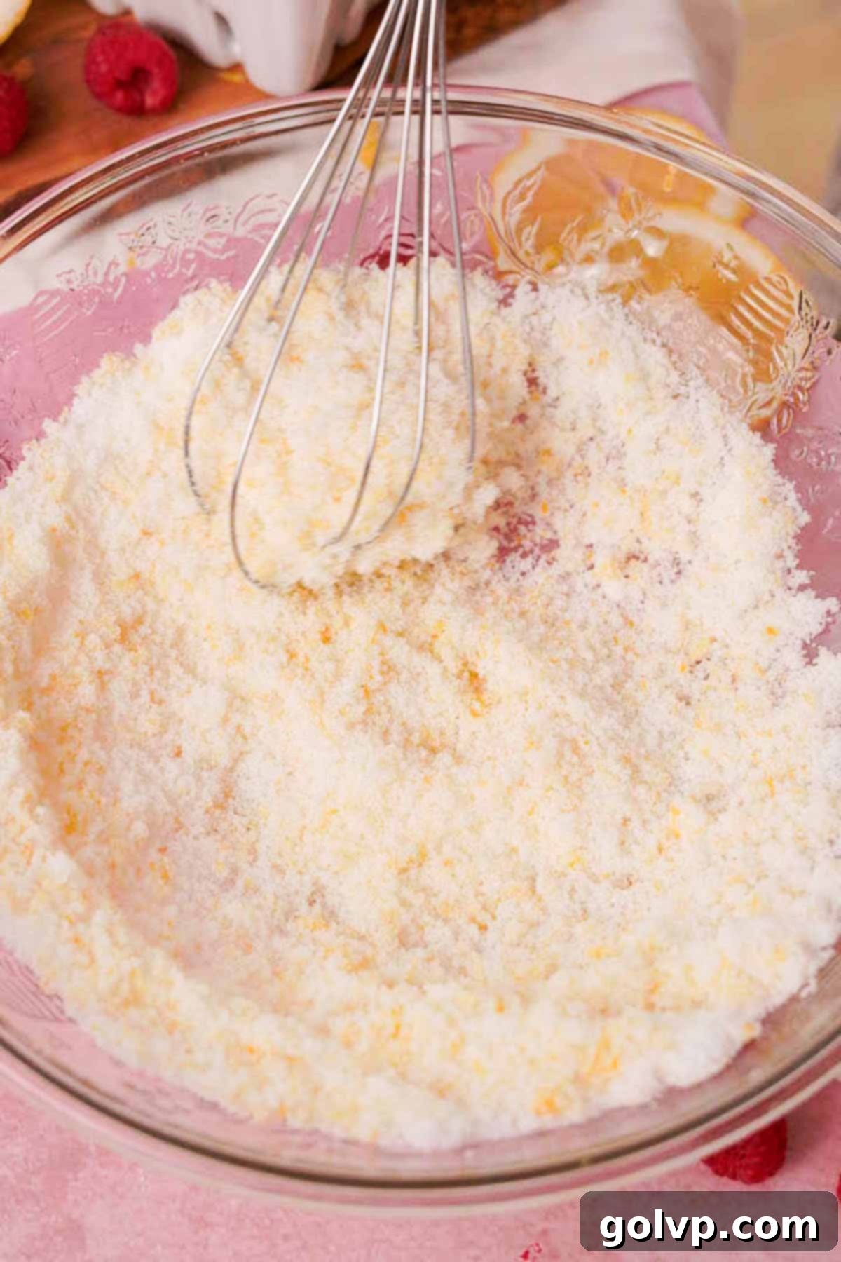 A large glass bowl with bright yellow lemon zest and granulated sugar being vigorously whisked together by hand