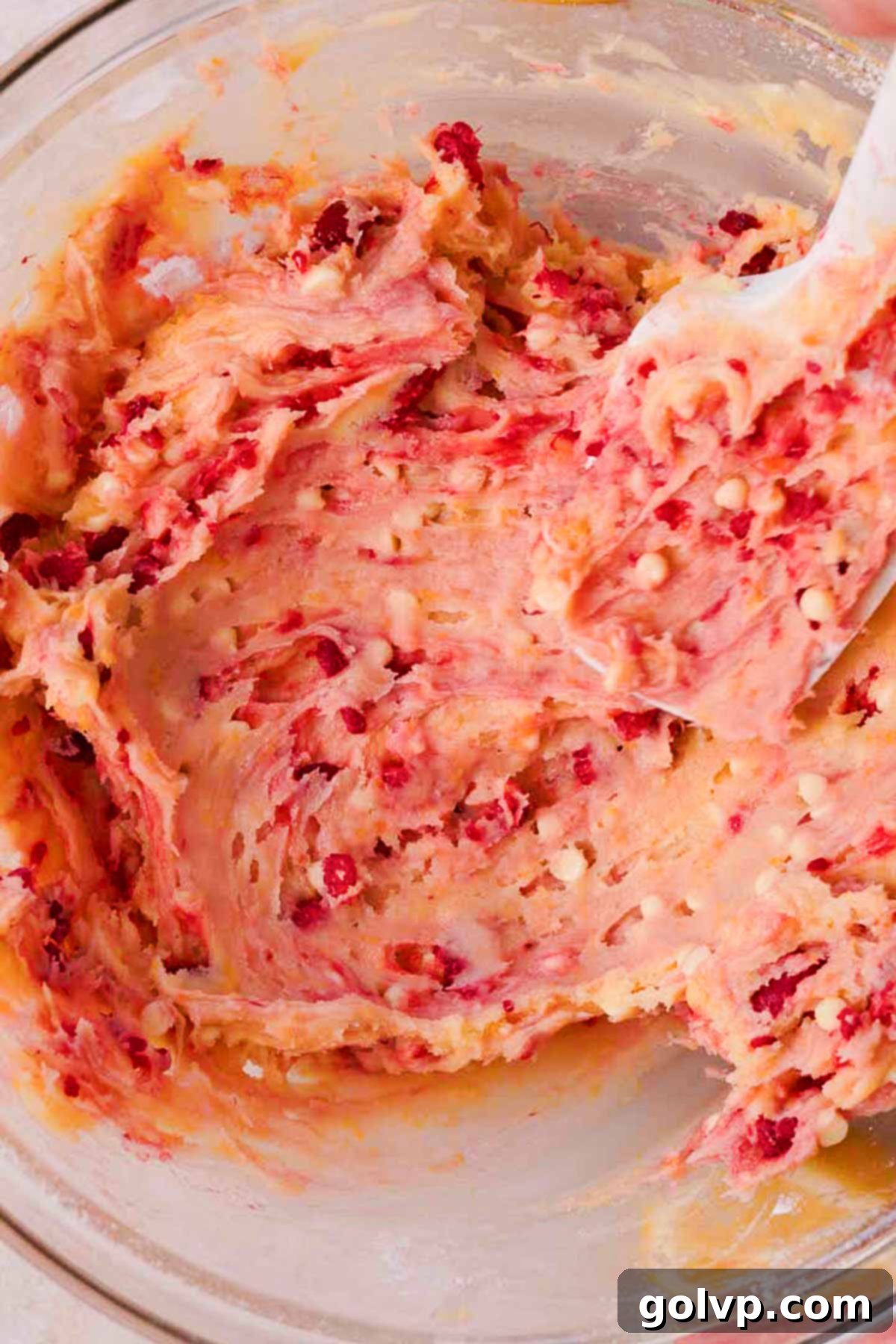 Gently folding lemon raspberry cookie dough with a spatula in a large glass bowl, creating beautiful streaks and swirls of raspberry