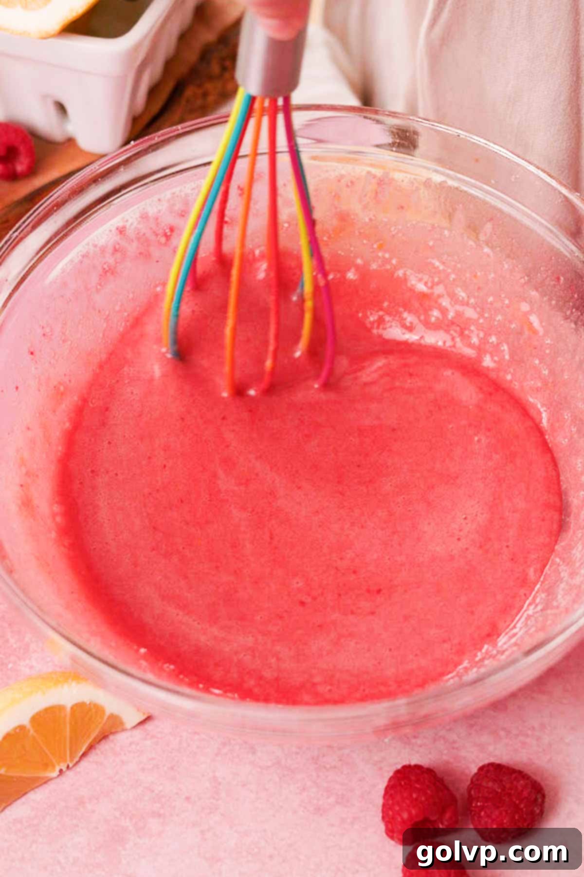 Stirring the creamy filling for raspberry bars in a large glass bowl with a whisk, incorporating the raspberry puree and lemon juice.
