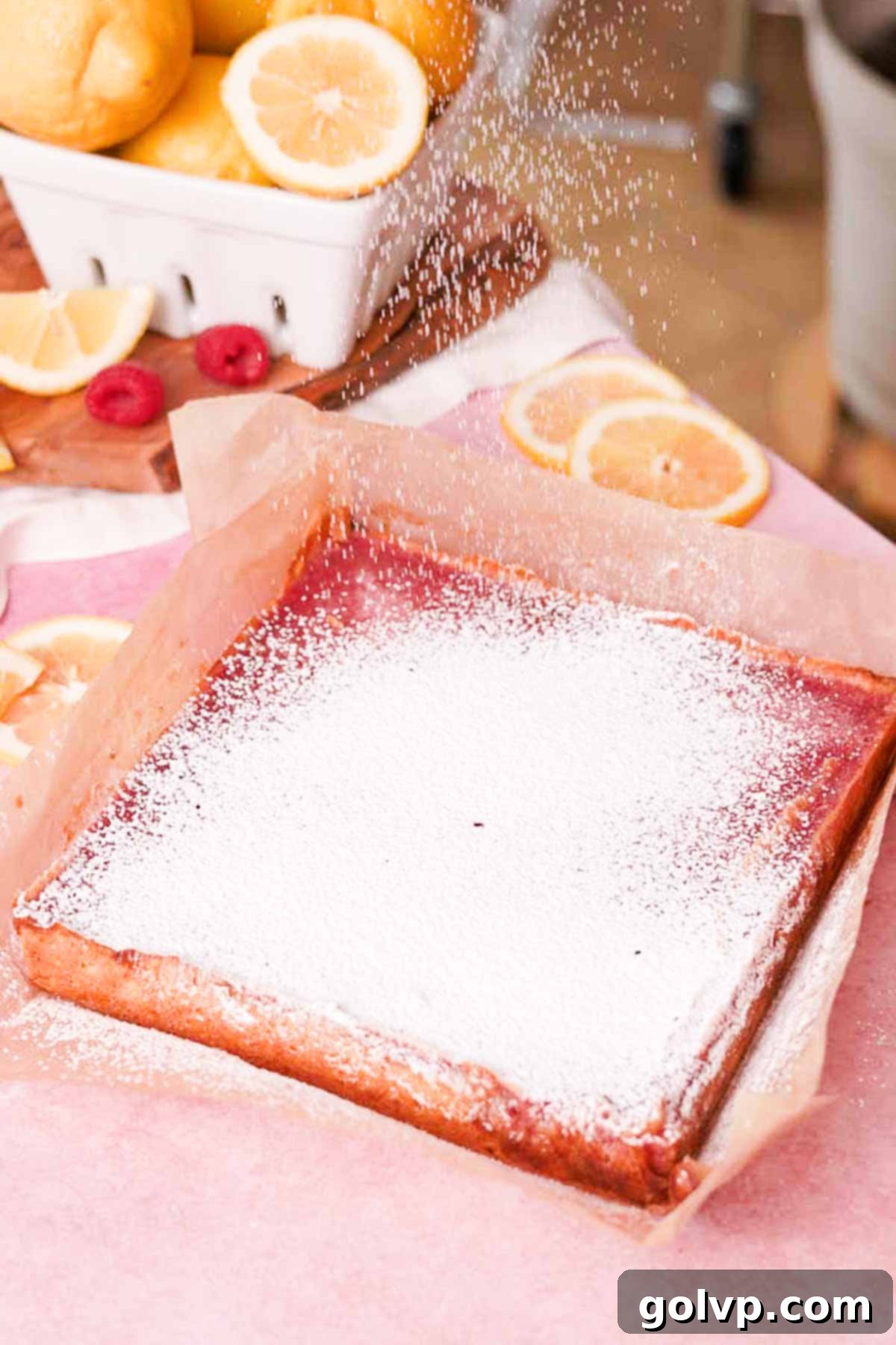 Sprinkling finished lemon raspberry bars with powdered sugar before serving, highlighting their beautiful color.
