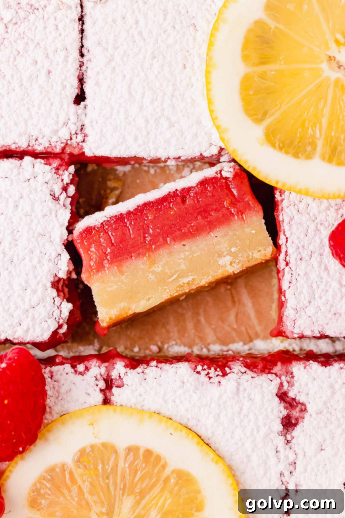 Top view of lemon raspberry bars with one bar turned on its side to show the thick gooey filling and buttery shortbread crust.