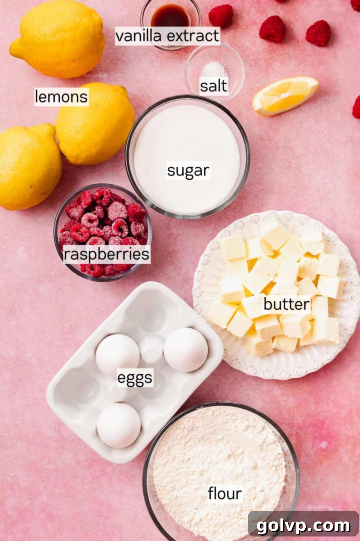 Arrangement of lemon raspberry bar ingredients in various glass bowls and plates, including fresh lemons, raspberries, flour, butter, and sugar.