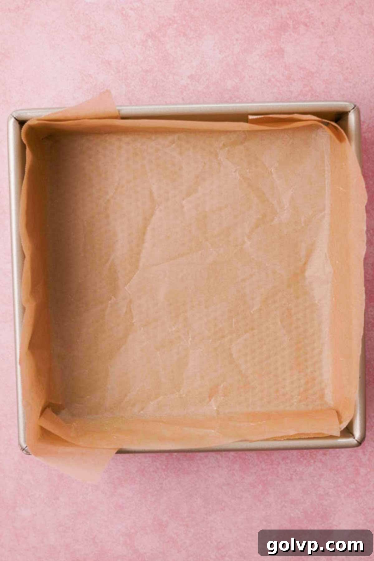 Square baking pan completely lined with parchment paper, perfectly fitted for the shortbread crust.