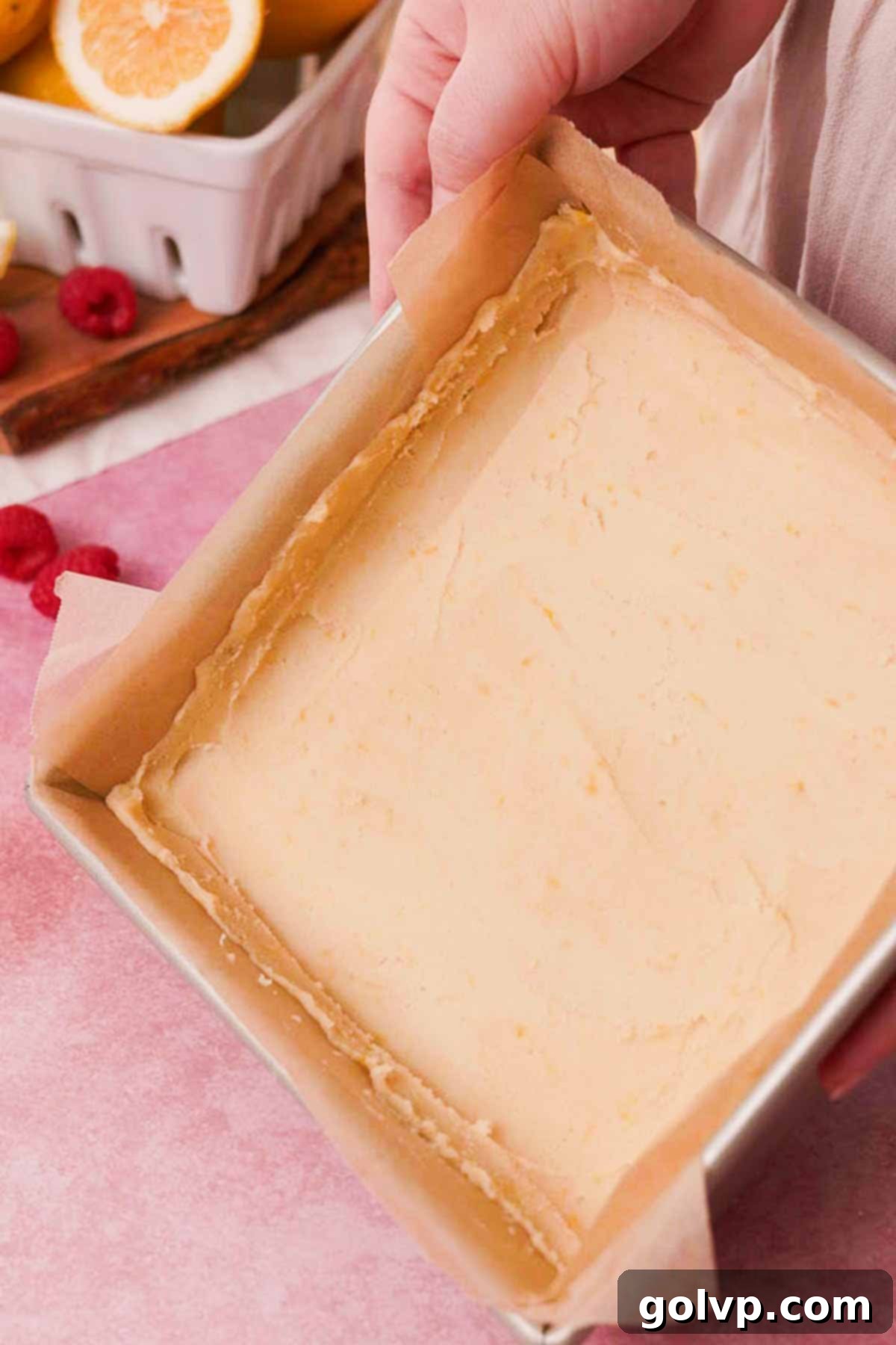 Smoothing shortbread crust into a square parchment-lined baking pan, creating an even base with raised edges.
