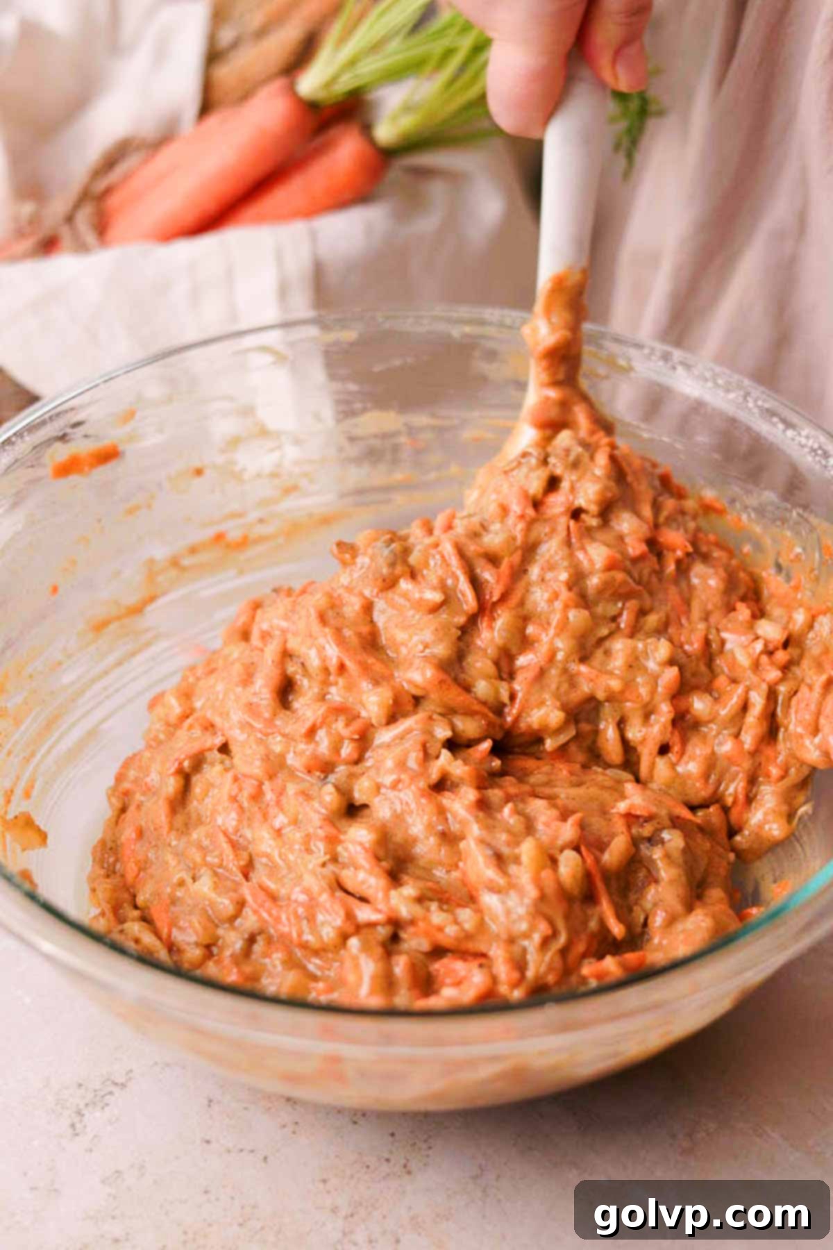 folding carrot cake batter in large glass bowl with a rubber spatula