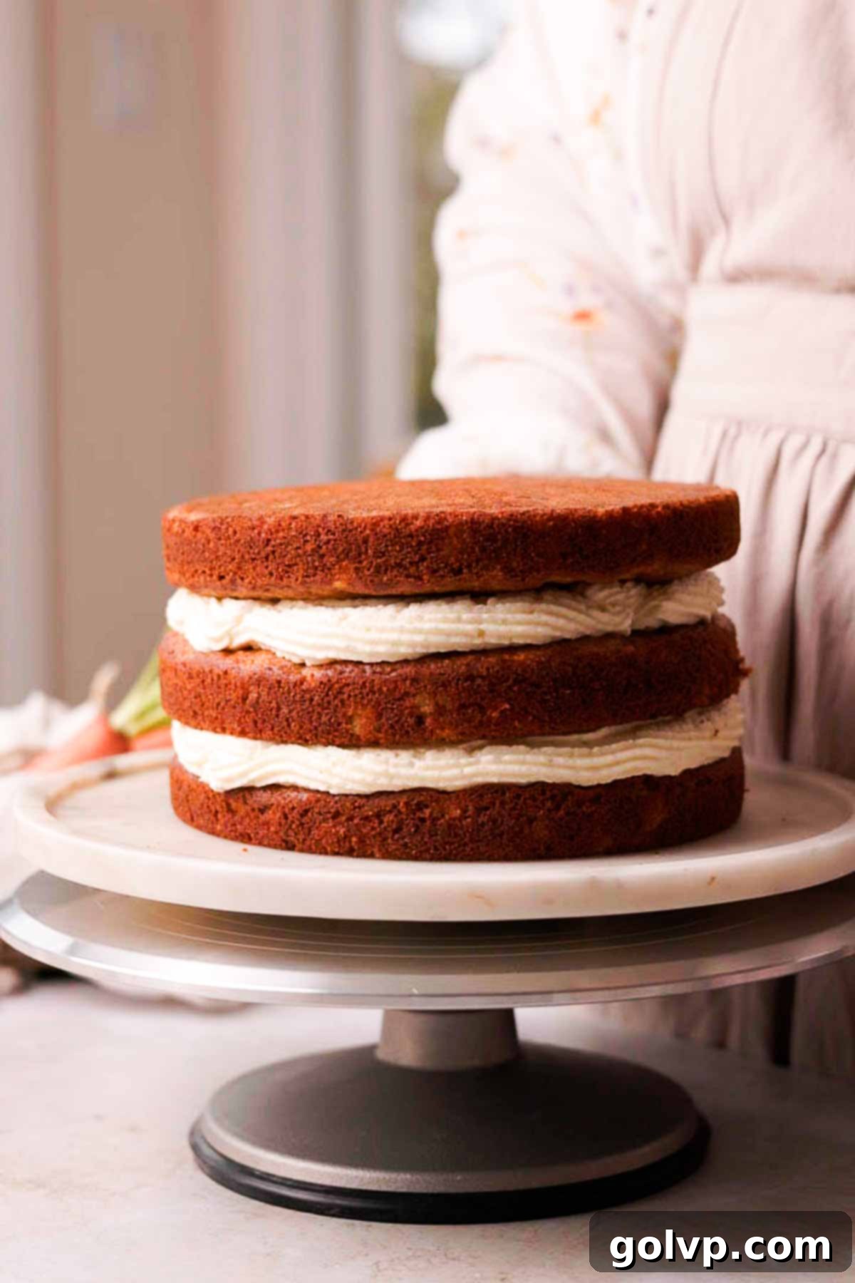 stacked cake layers with cream cheese frosting on a turntable
