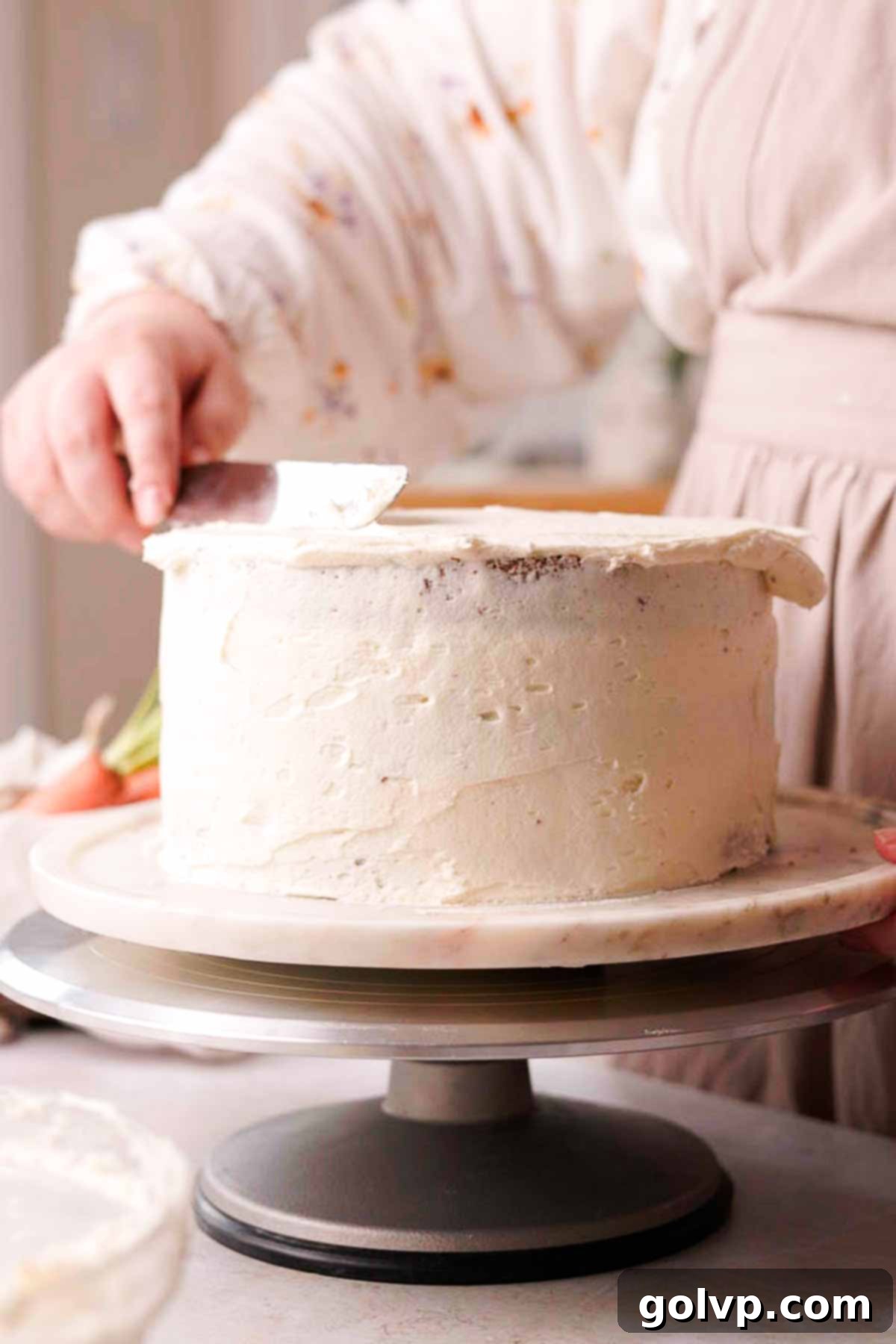 covering carrot cake with frosting and scraping with long metal spatula