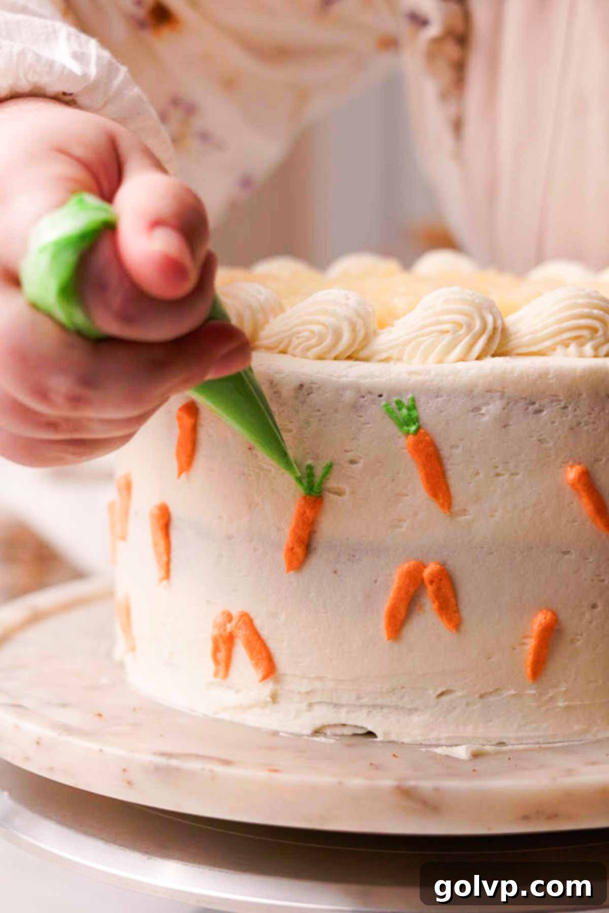 piping green leaves onto mini orange carrots on the side of a frosted carrot cake