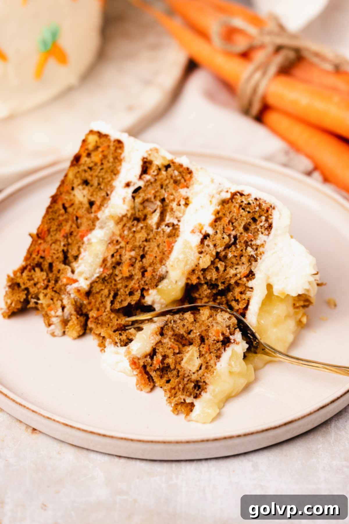fork taking a bite from a slice of carrot cake with pineapple and pineapple filling on a plate