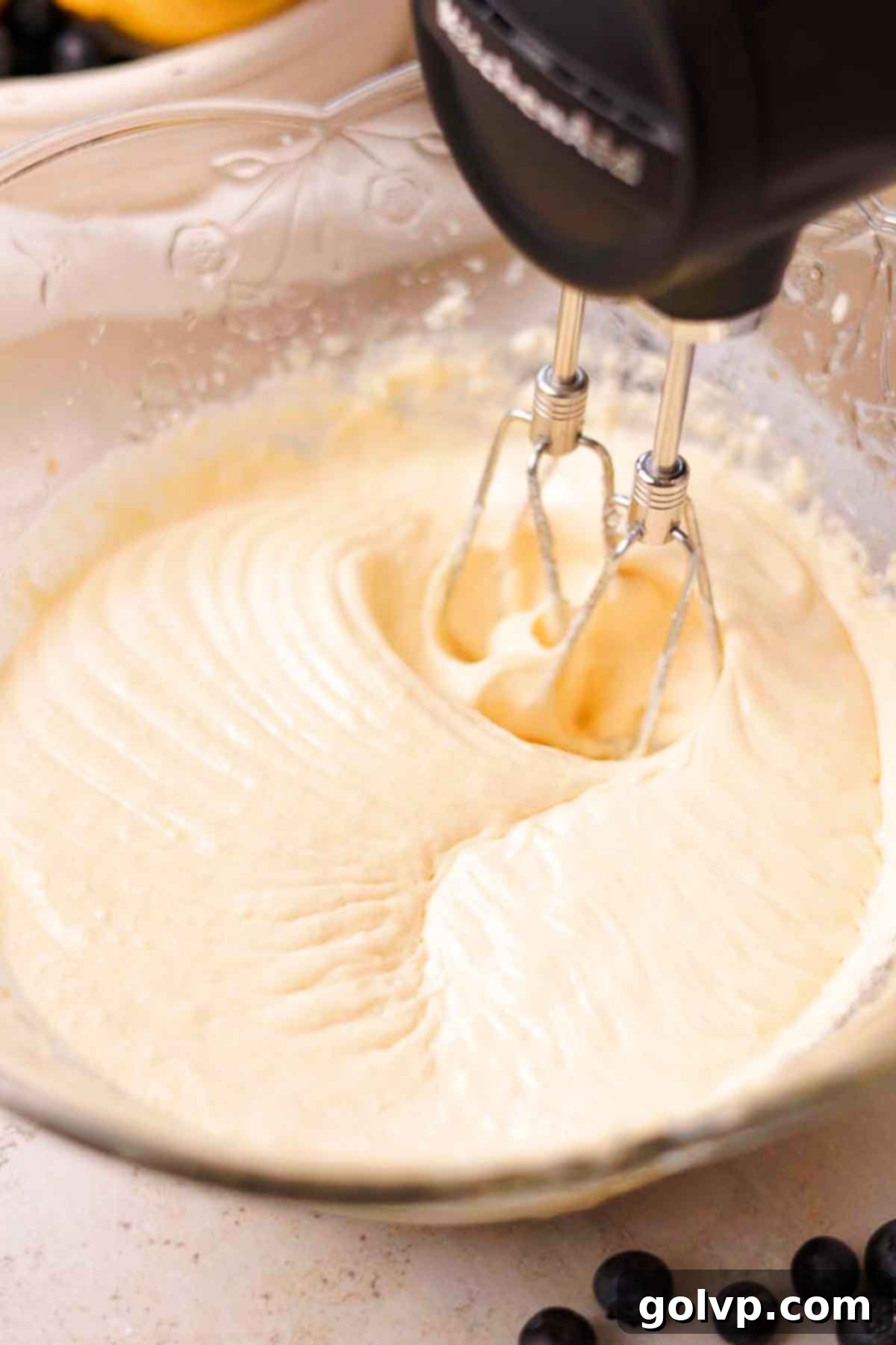 Combining wet ingredients for blueberry lemon cake batter, including eggs, vanilla, lemon juice, and sour cream, in a large glass bowl.