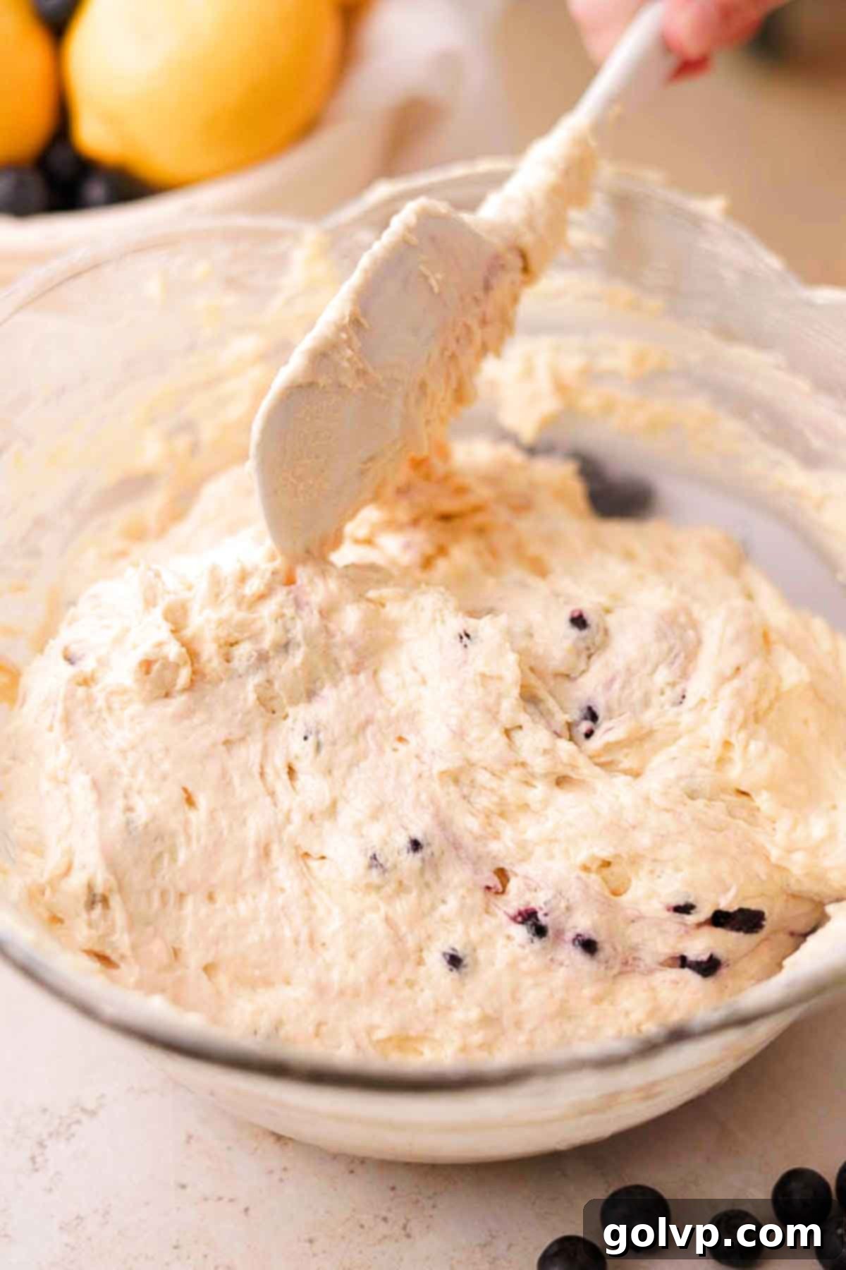 Gently folding the floured blueberries into the lemon cake batter with a silicone spatula.