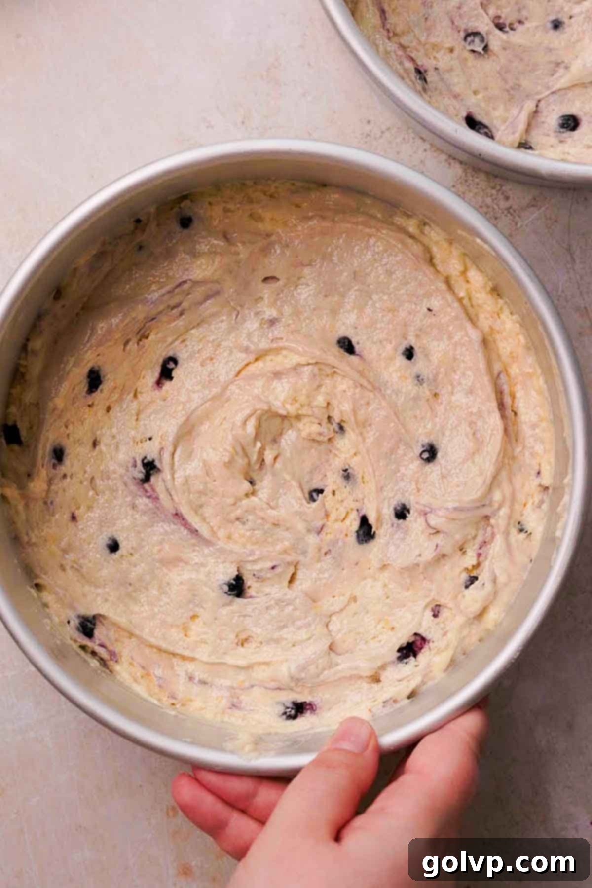 Blueberry lemon cake batter in an eight-inch round baking pan, ready to go into the oven.