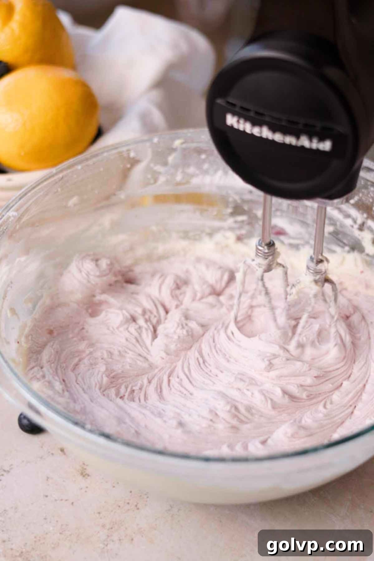 Beating pale blue lemon blueberry cream cheese frosting with an electric mixer, demonstrating its smooth texture.