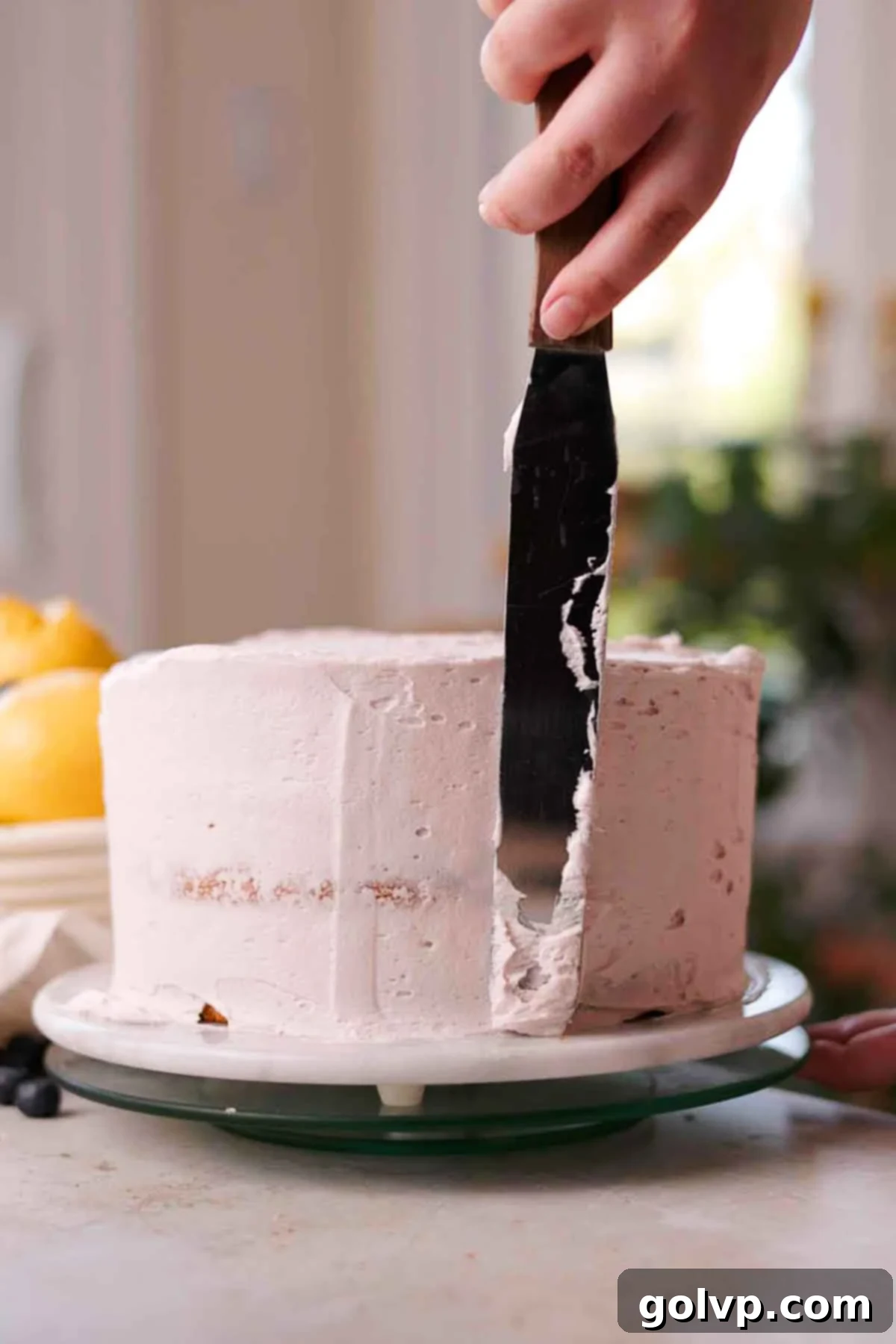 Spreading blueberry lemon cream cheese frosting evenly over the outside of the layered cake with an offset spatula, creating a smooth finish.