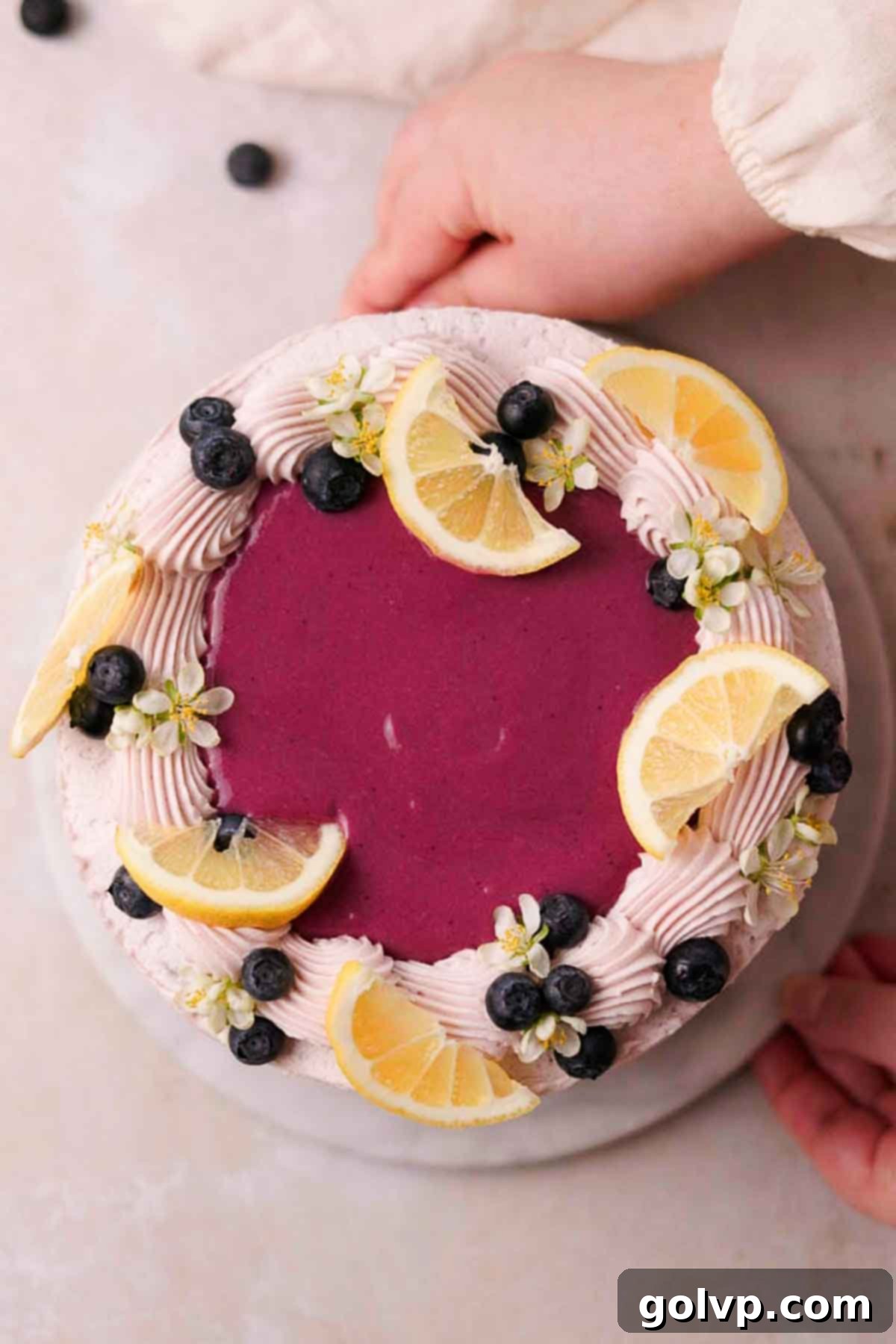 Decorated cake top with a pool of blueberry curd, fresh lemon wedges, edible blossom flowers, and fresh blueberries, creating a vibrant display.