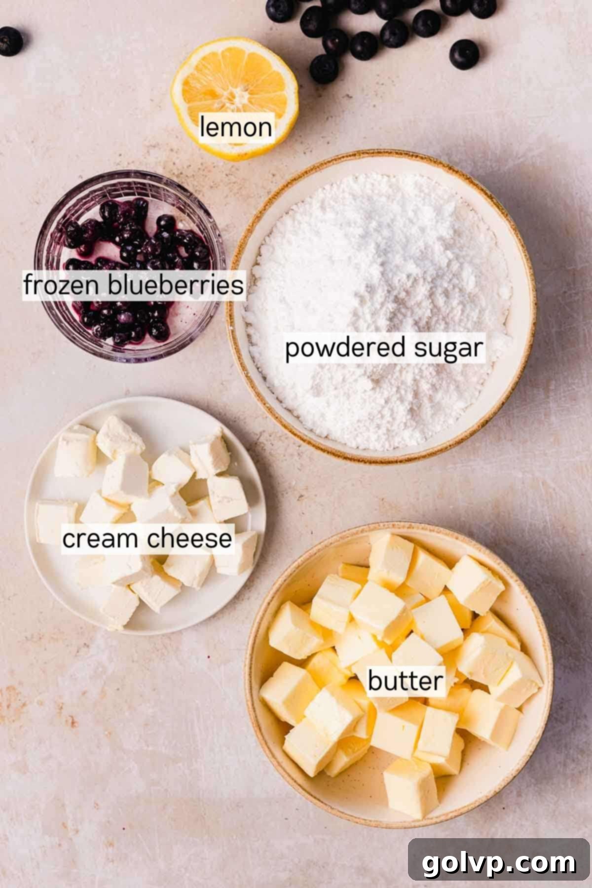 Bowls of ingredients for blueberry lemon cream cheese frosting: softened butter, powdered sugar, cream cheese, lemon juice, and thawed wild blueberries.