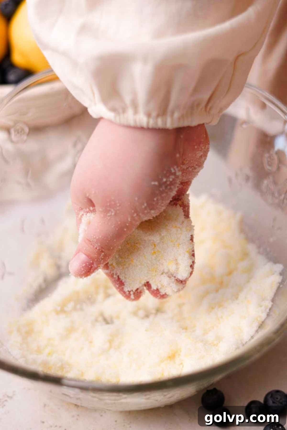 Rubbing lemon zest and granulated sugar together with fingers in a large glass bowl to release aromatic oils.