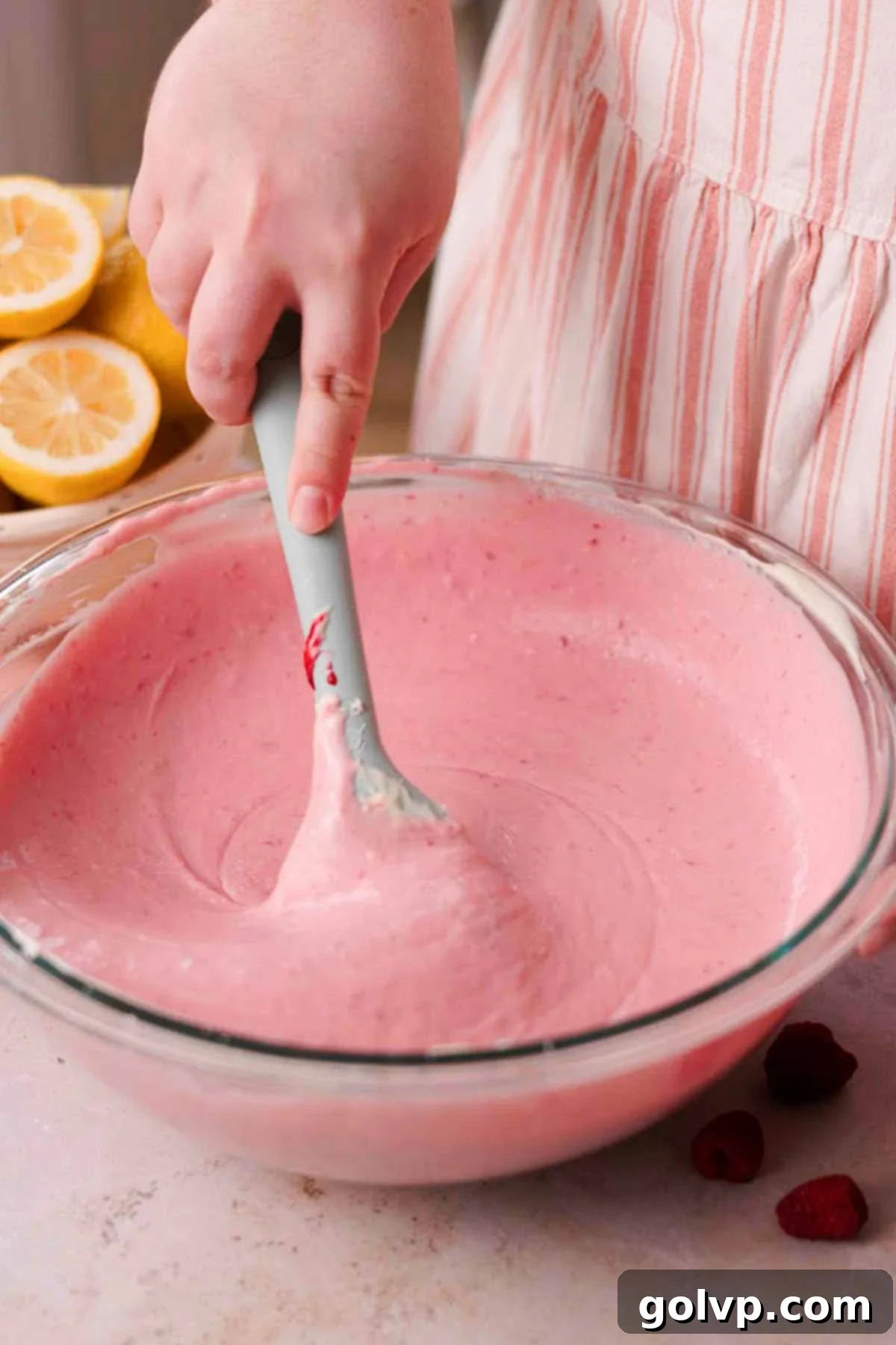 stirring lemon raspberry cheesecake batter with blue rubber spatula