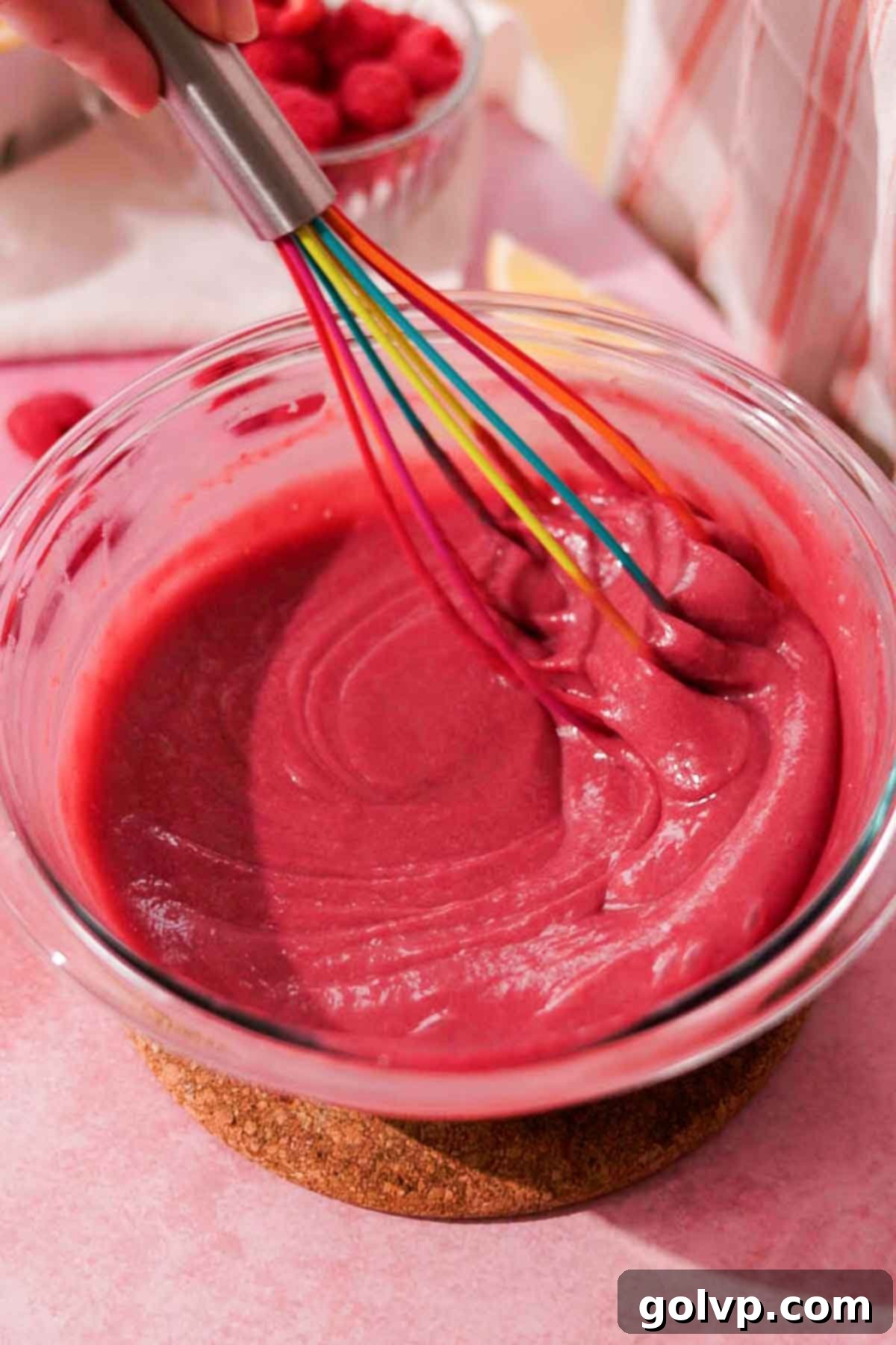 whisking raspberry curd in large bowl with silicone whisk