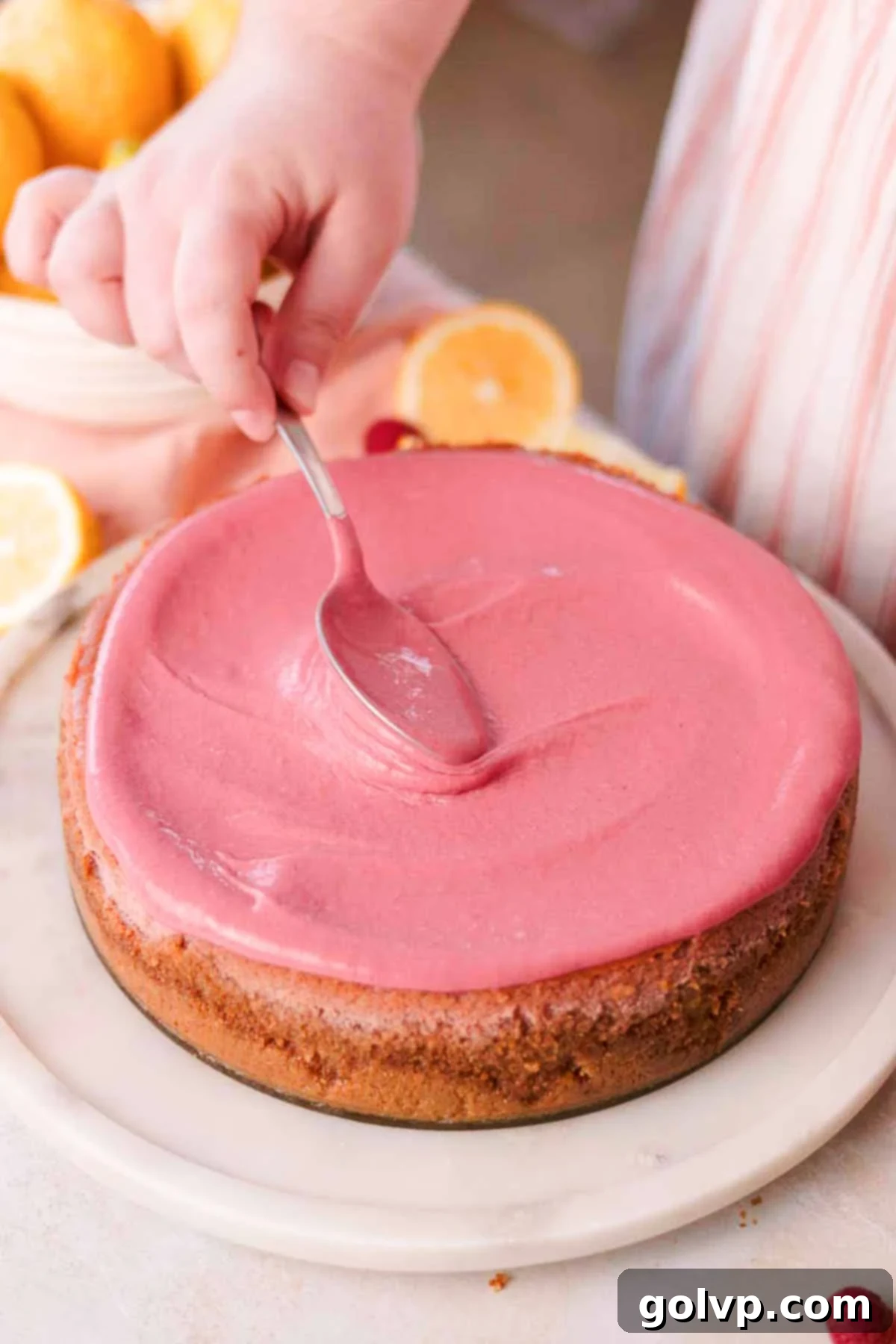spreading raspberry curd on top of baked and cooled cheesecake with the back of a spoon