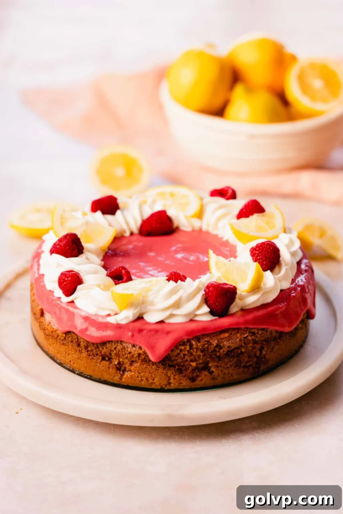 cheesecake topped with raspberry curd, whipped cream, lemon wedges, and fresh raspberries