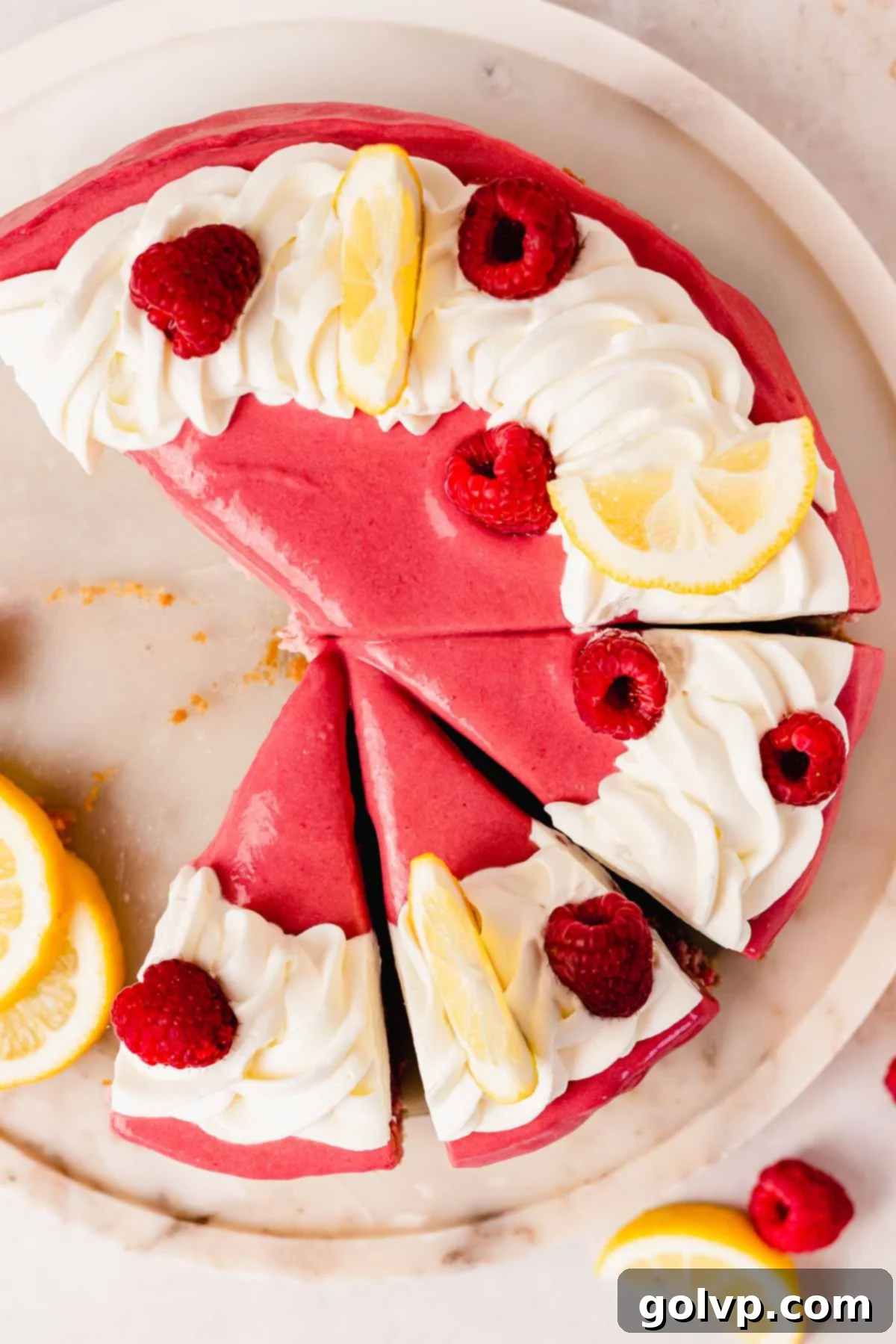 sliced lemon raspberry cheesecake with whipped cream swirl, lemon wedges, and whole raspberries