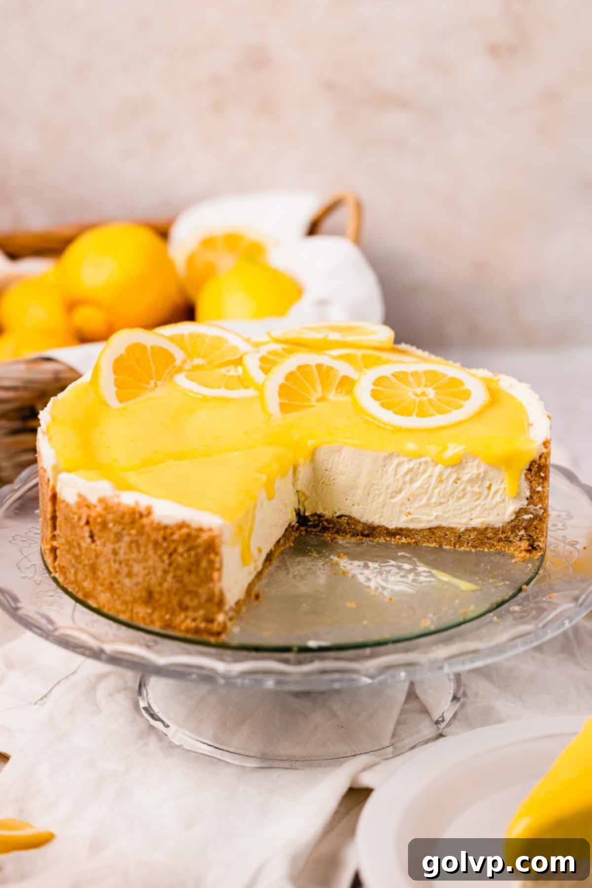 lemon curd cheesecake on glass cake stand topped with lemon curd with a wedge cut out