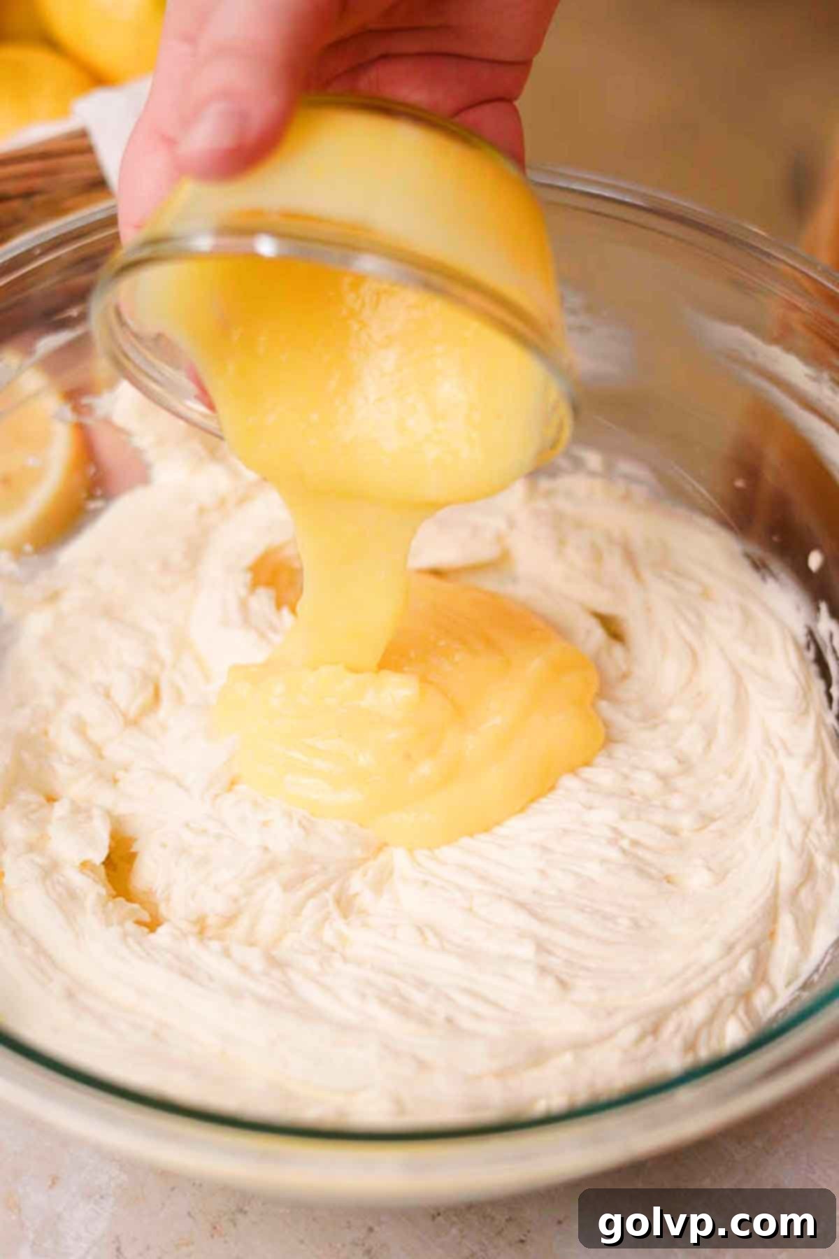 pouring lemon curd into lemon cheesecake filling