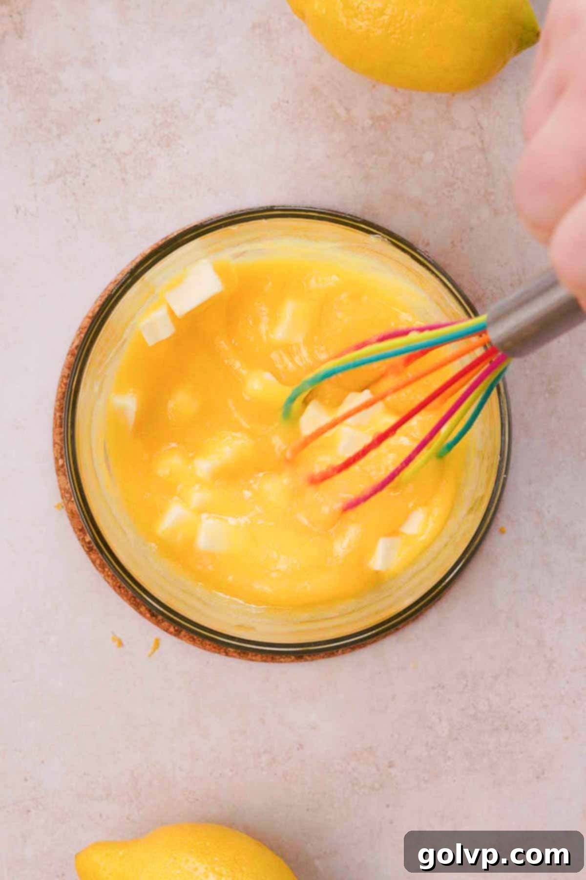whisking cooked lemon curd in glass bowl with cold butter