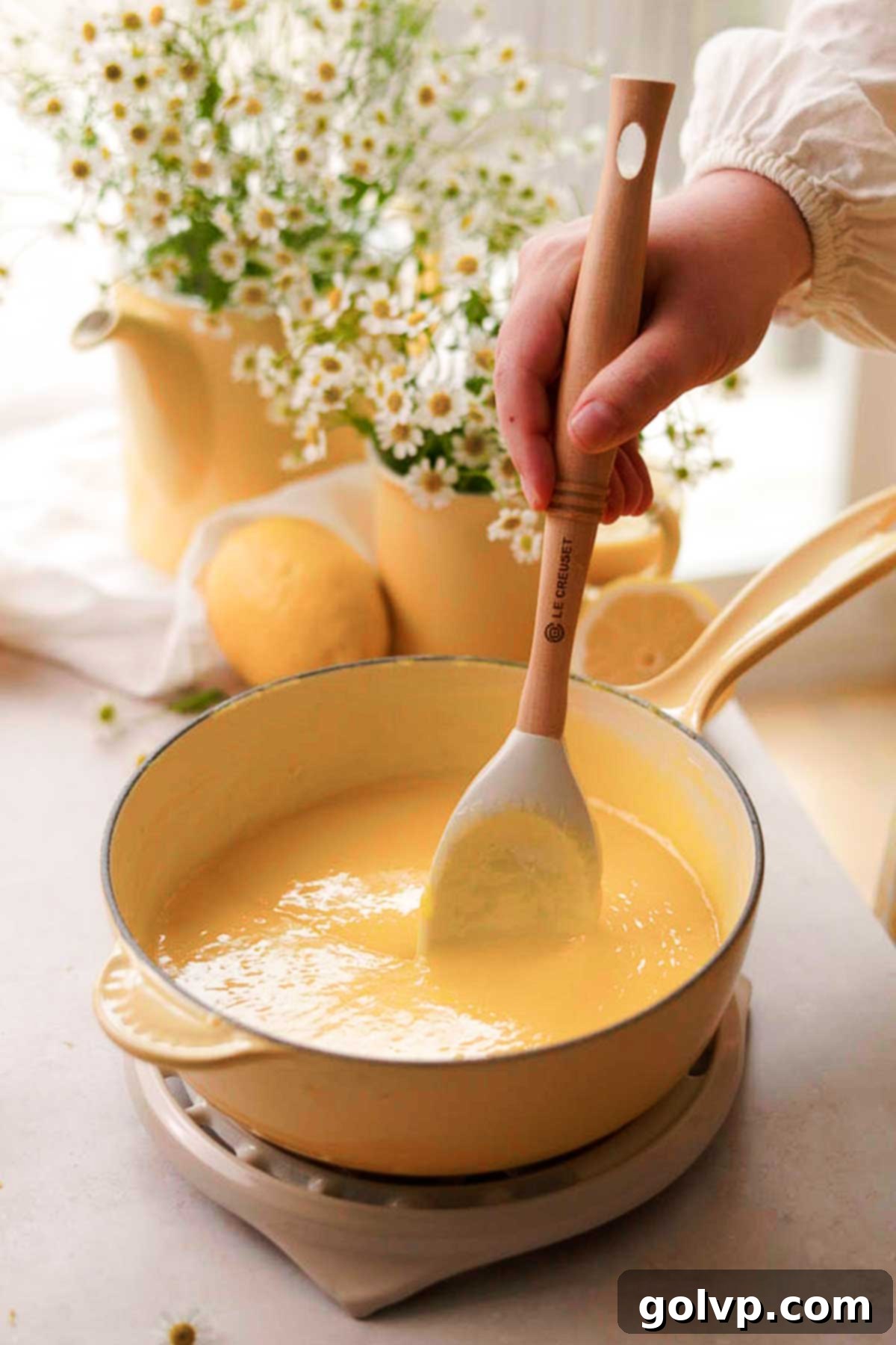 A spatula stirring softened butter into the freshly cooked hot lemon curd, creating a smooth and glossy finish.