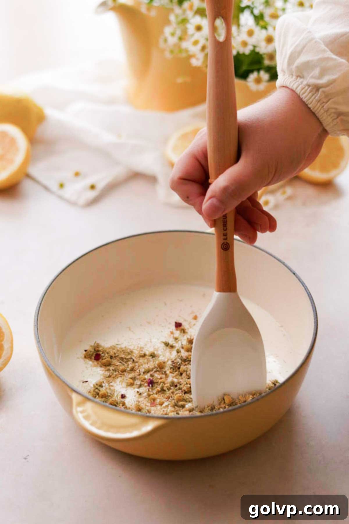 Adding and stirring chamomile tea into a pot of heavy cream on low heat, initiating the infusion process.