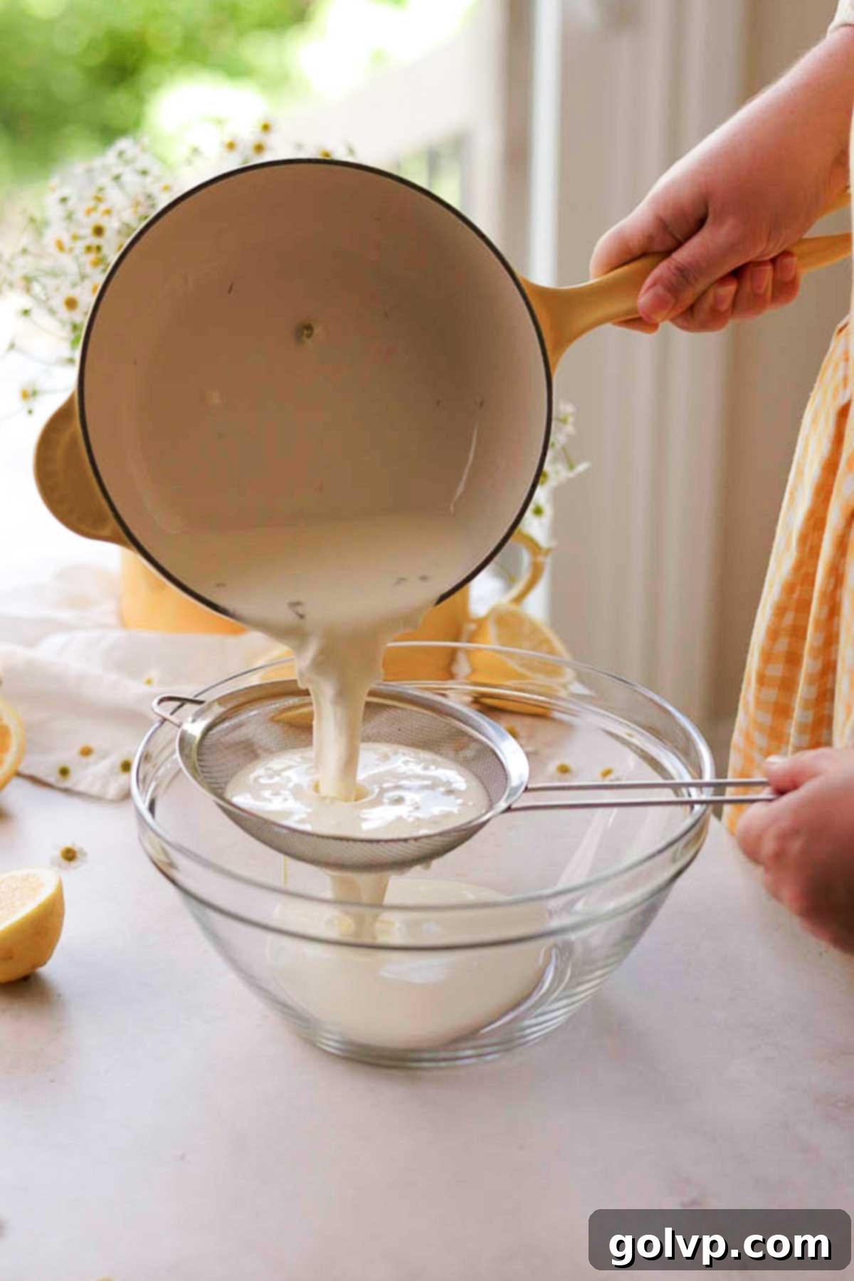 Straining the chamomile tea out of the infused heavy cream into a clean bowl, preparing it for chilling.
