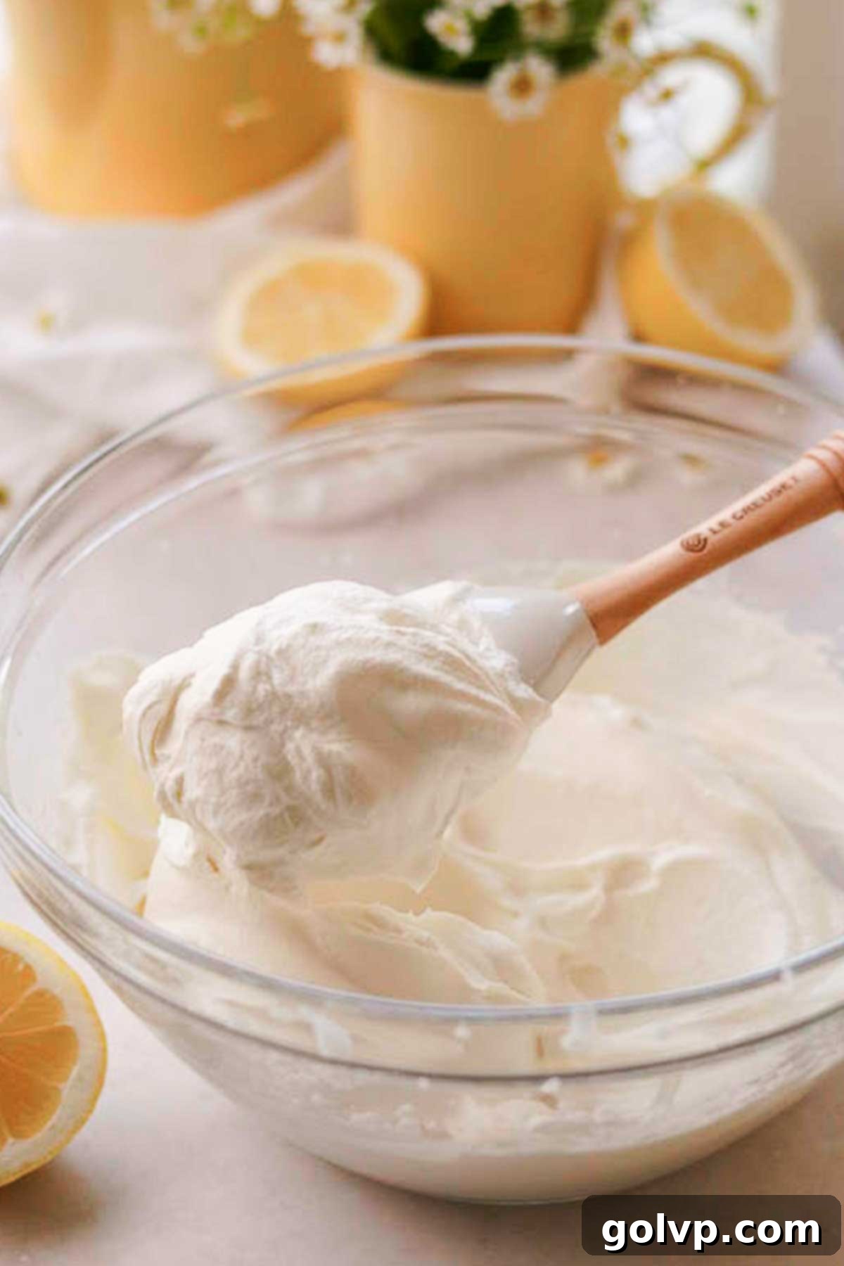 A bowl of freshly whipped cream with stiff peaks, showing its smooth and airy texture, ready to be spread onto the cake.