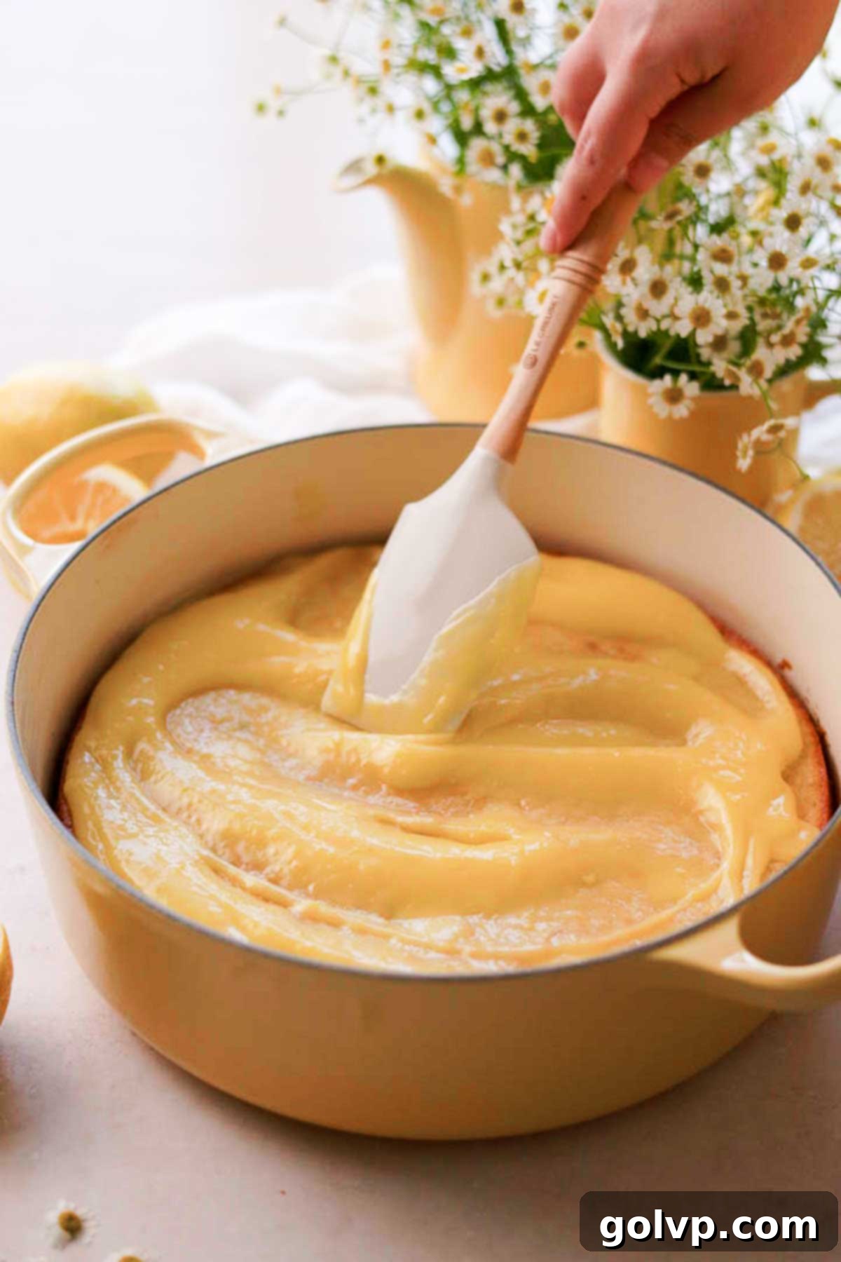 Spreading a generous layer of chilled lemon curd over the poked lemon cake, allowing it to seep into the holes.
