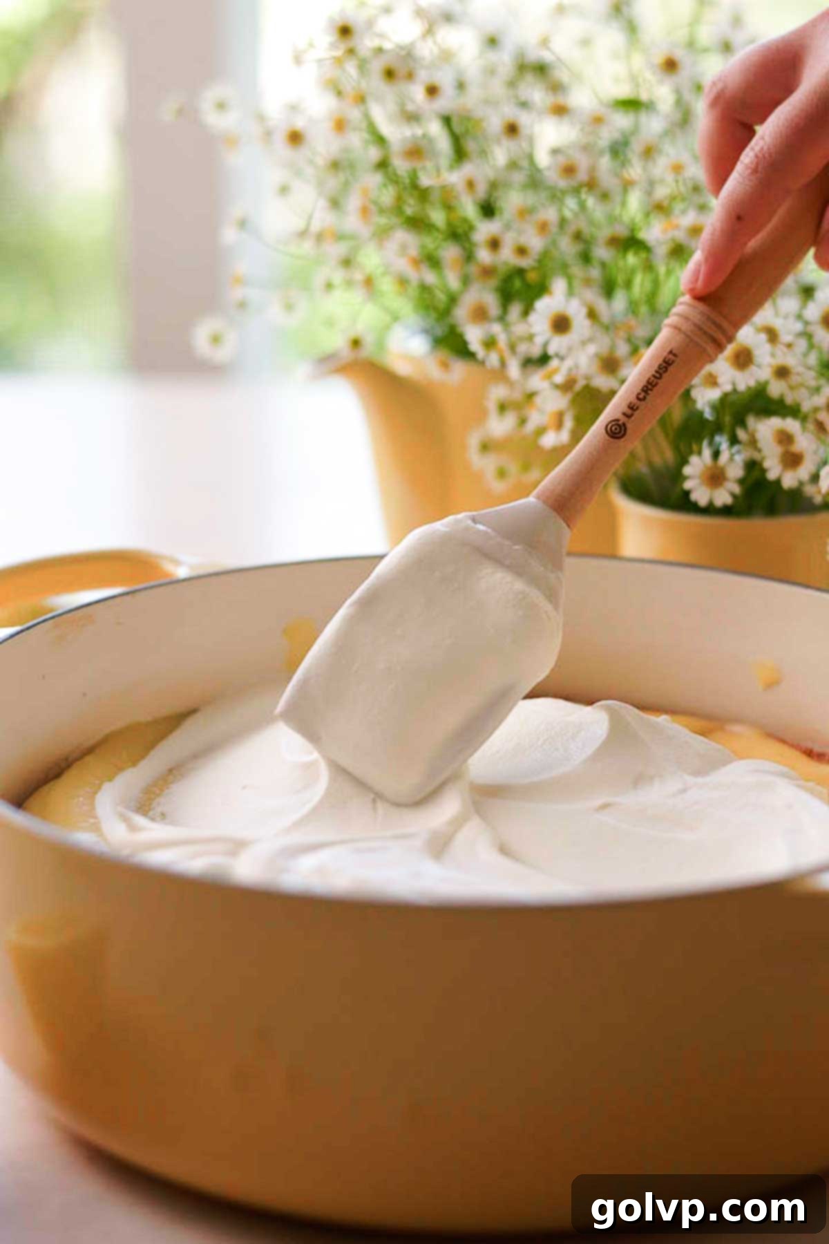 A smooth, even layer of chamomile-infused whipped cream being spread over the lemon curd-soaked cake, extending to the edges.