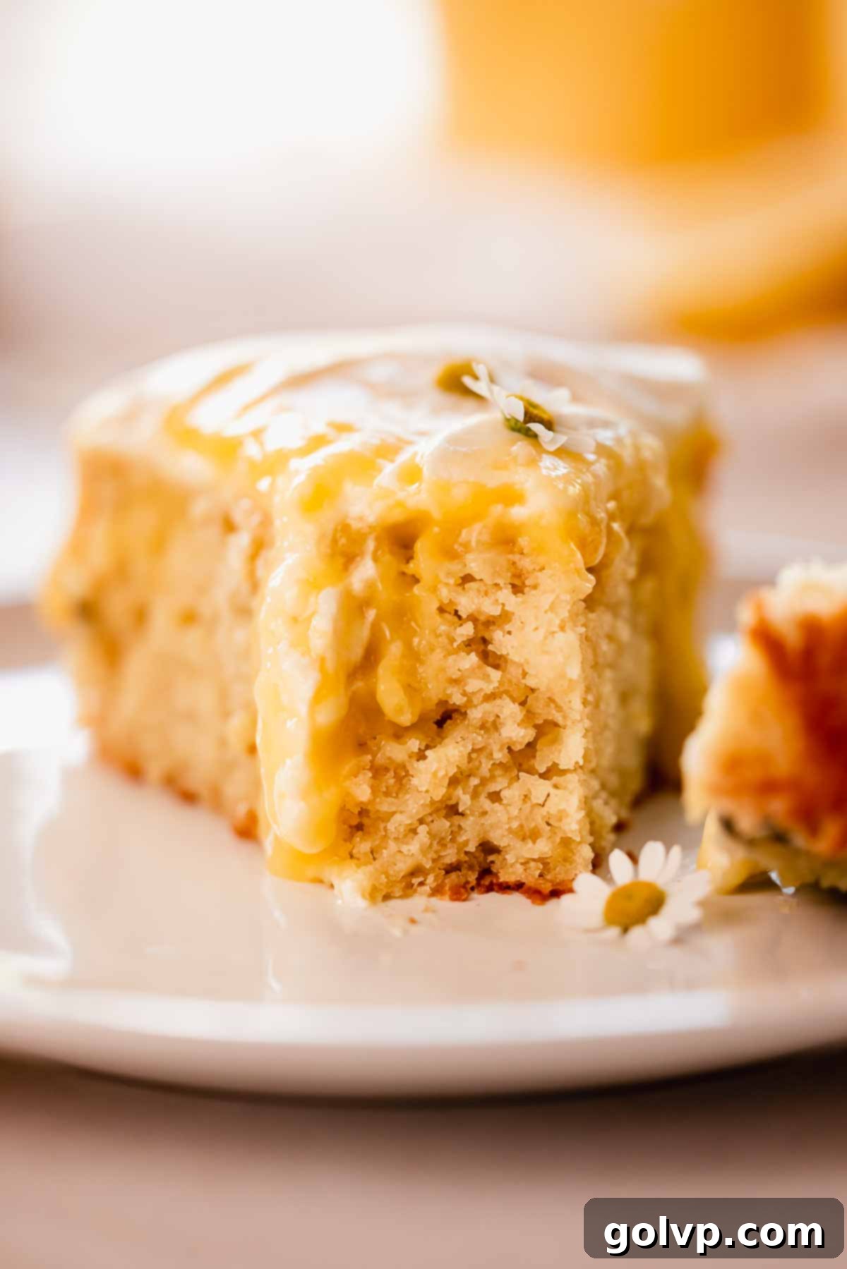A close-up view of a slice of lemon poke cake, showing its moist interior, pockets of lemon curd, and the airy whipped cream topping, with a small bite taken.