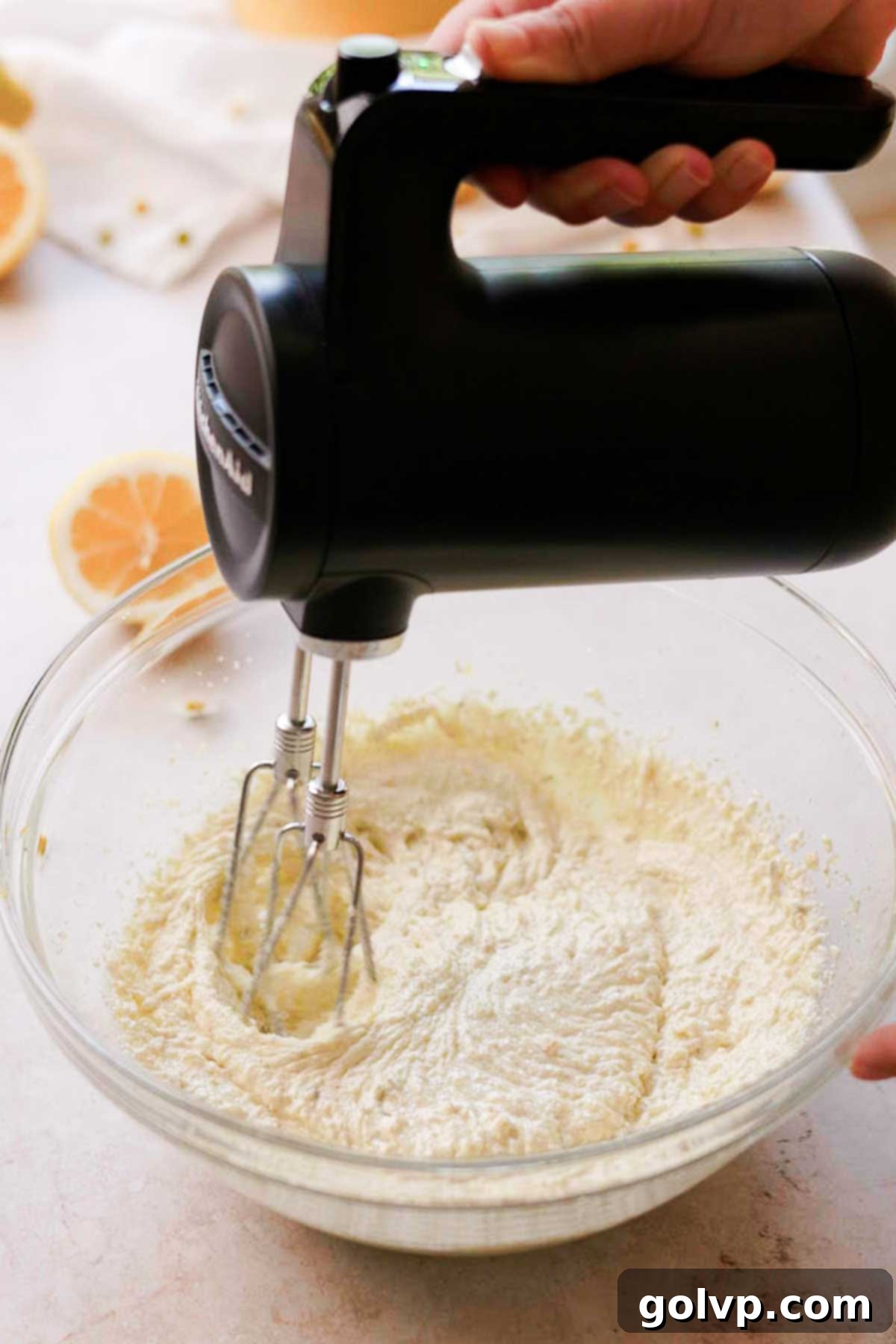 An electric hand mixer creaming together softened butter, olive oil, and the fragrant sugar mixture in a bowl until light and fluffy.