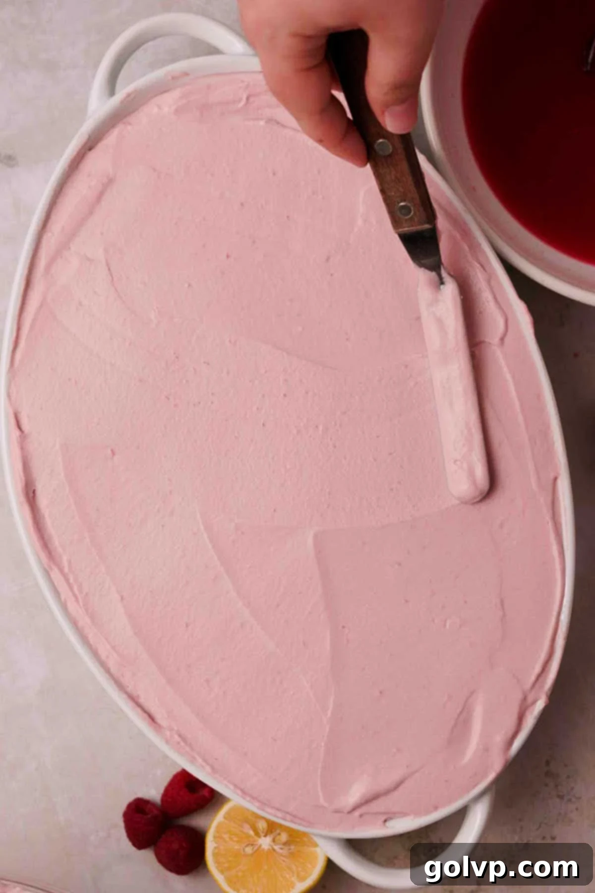 smoothing the top of raspberry tiramisu with an offset spatula