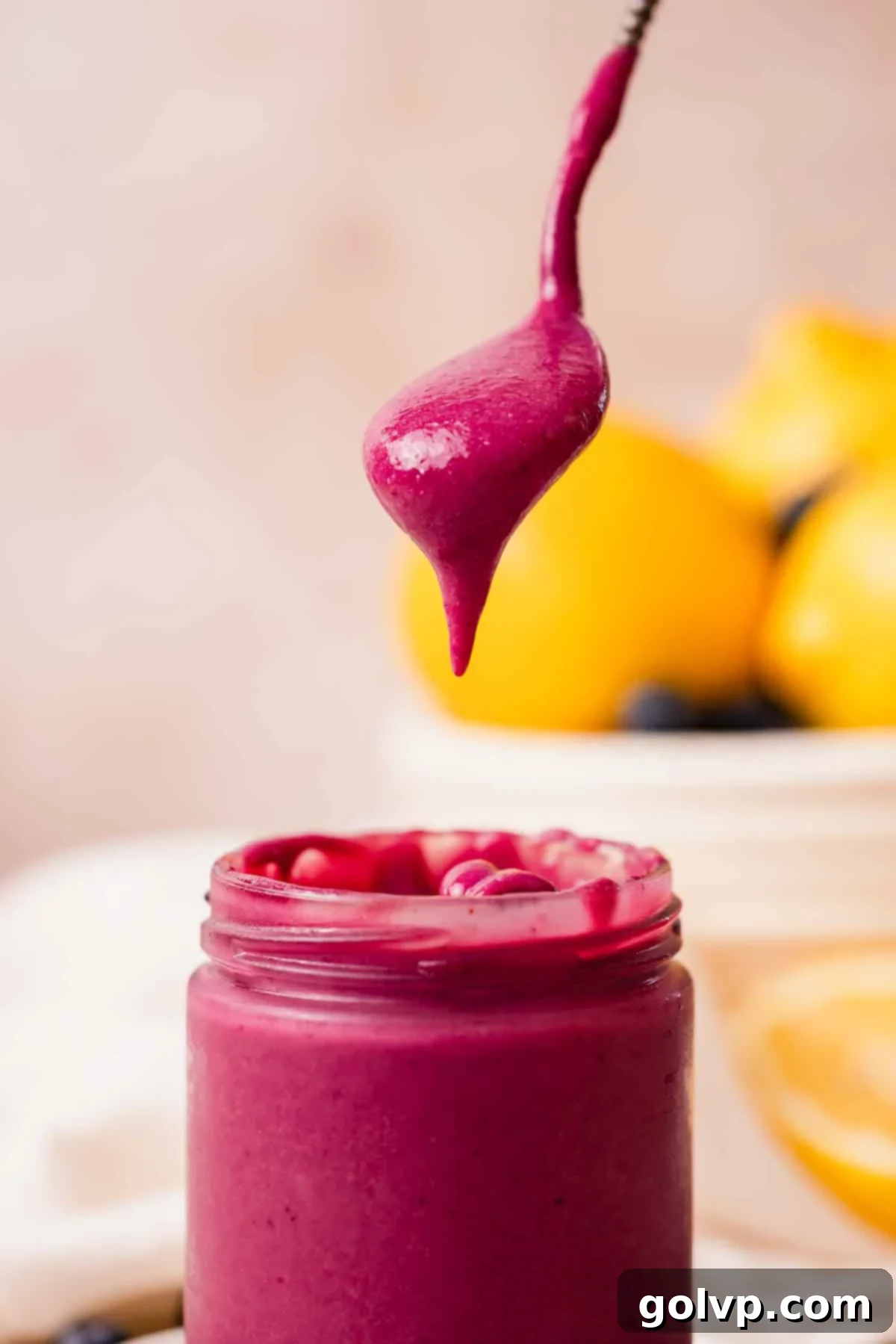 spoonful of bright purple blueberry curd held over a jar with it dripping down