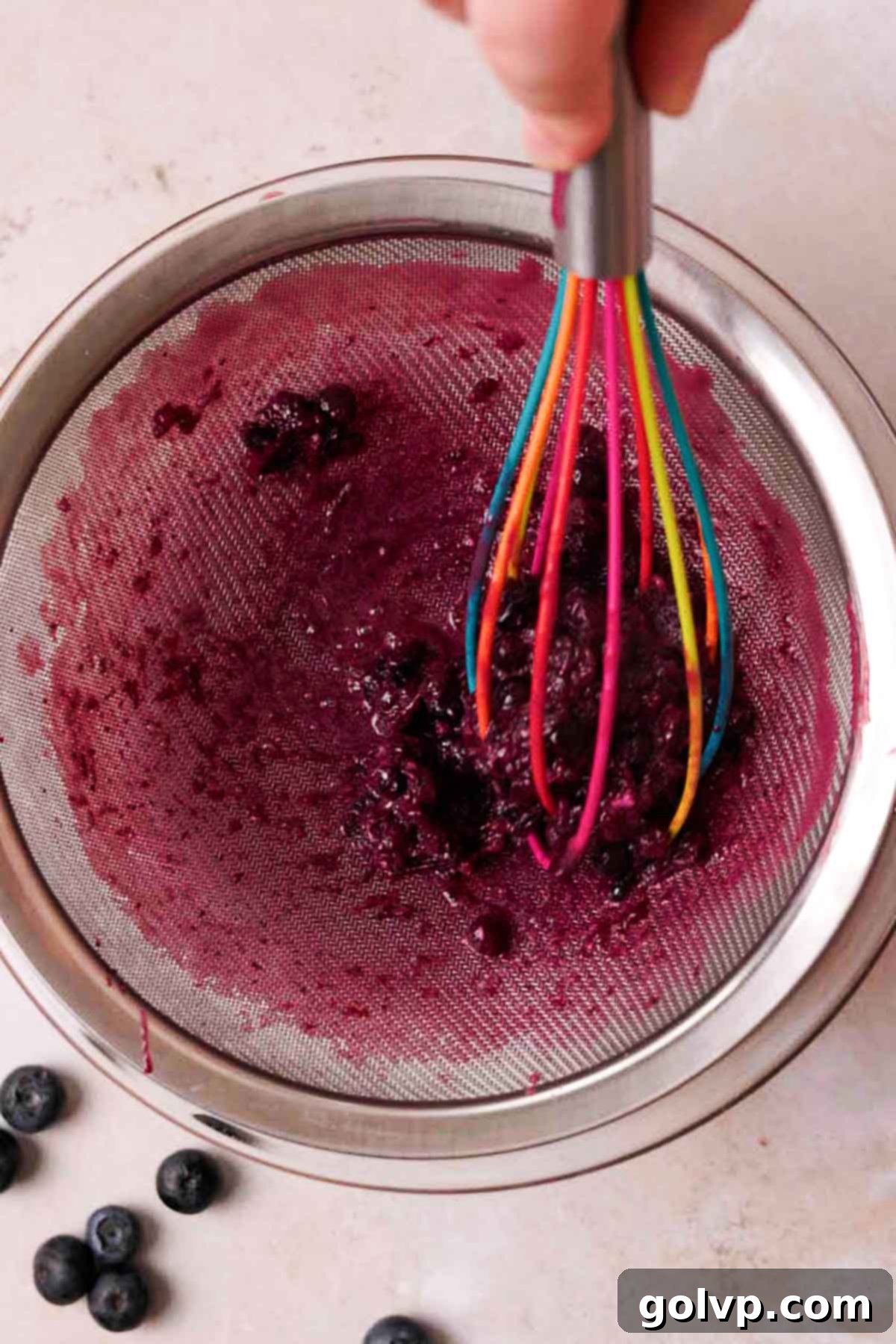 straining blueberry curd through mesh sieve into a glass bowl