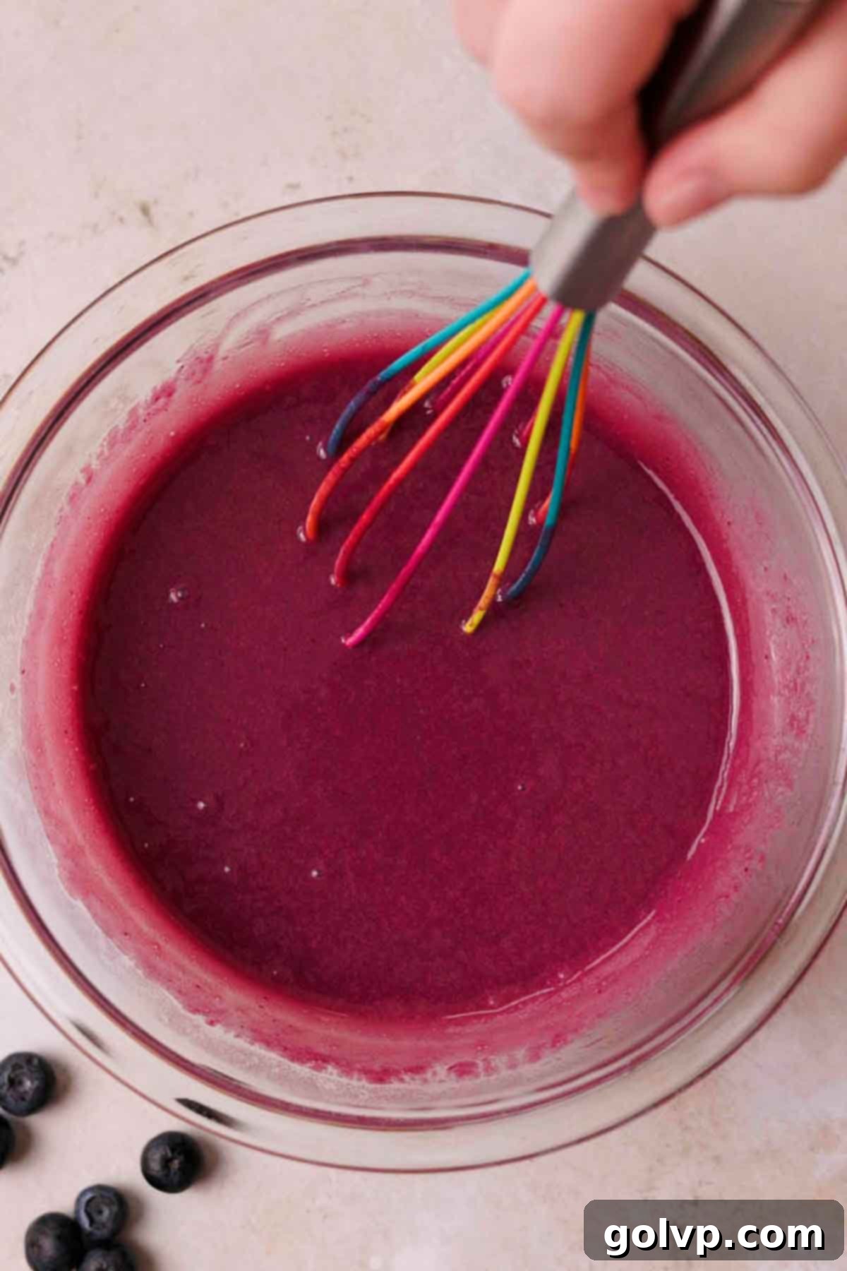whisking hot blueberry curd and butter in glass bowl with wire whisk
