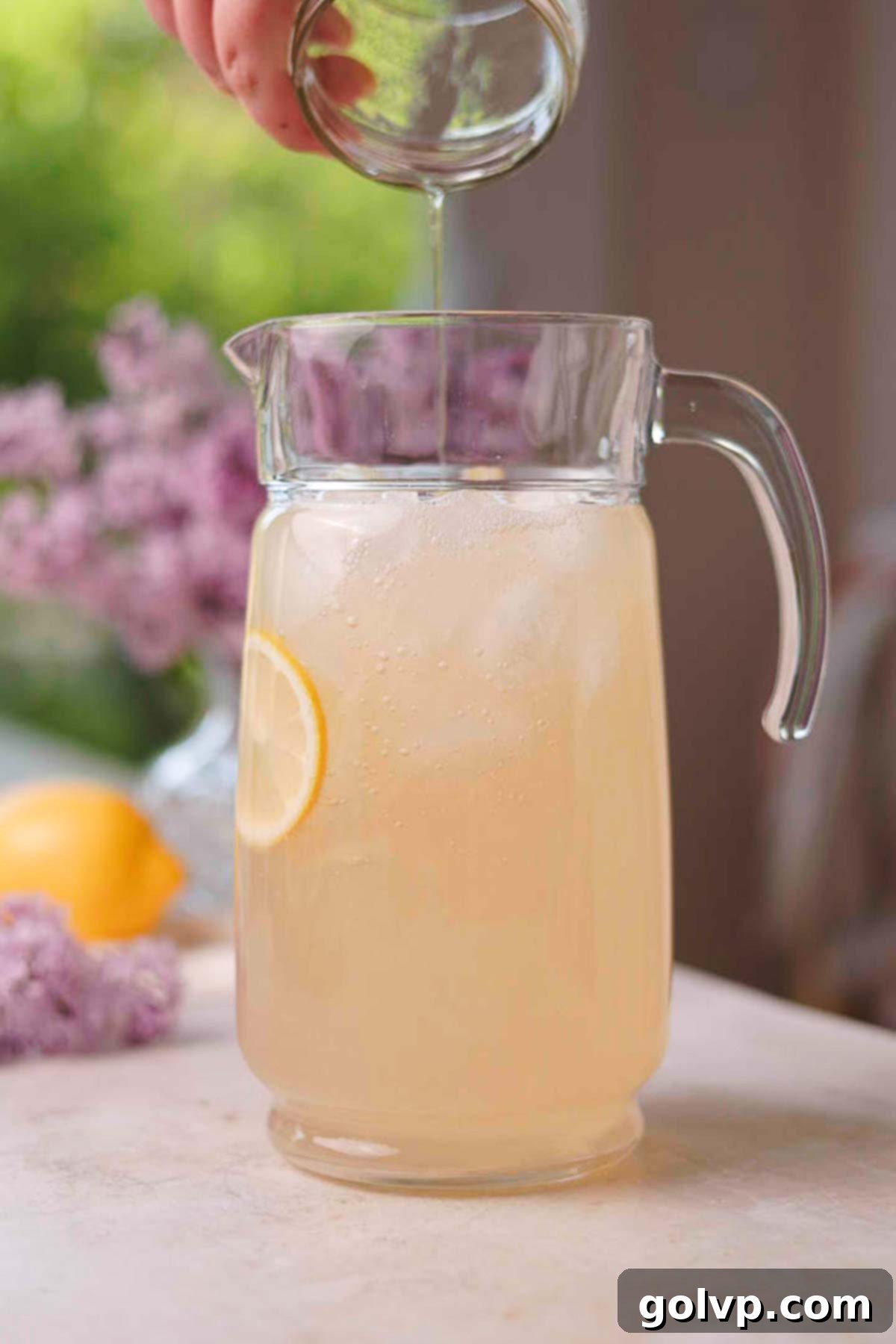 pouring lilac syrup into a pitcher full of lemon juice, water, and ice