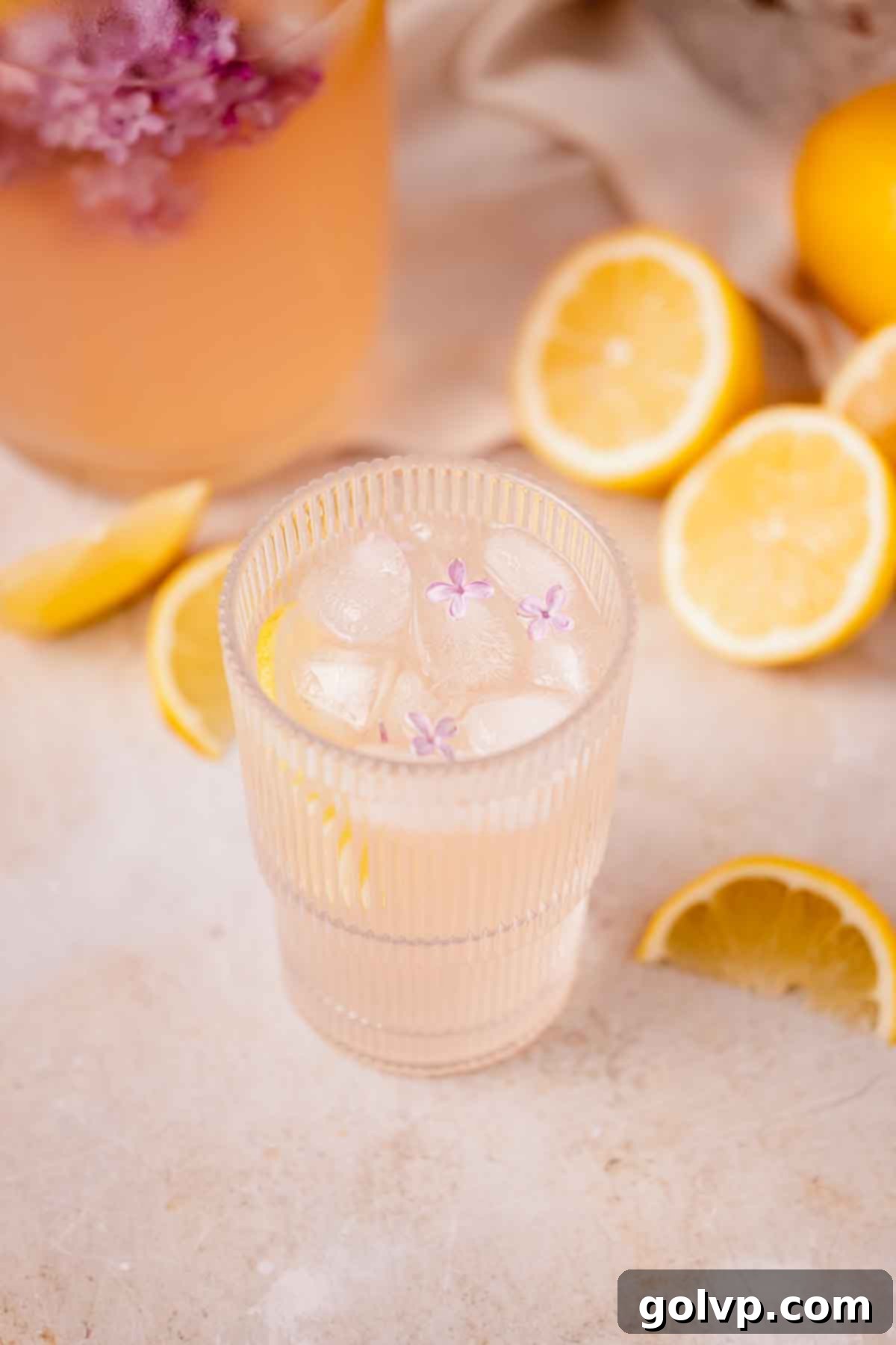 lilac lemonade in large glass with three small lilac blossoms on top of ice